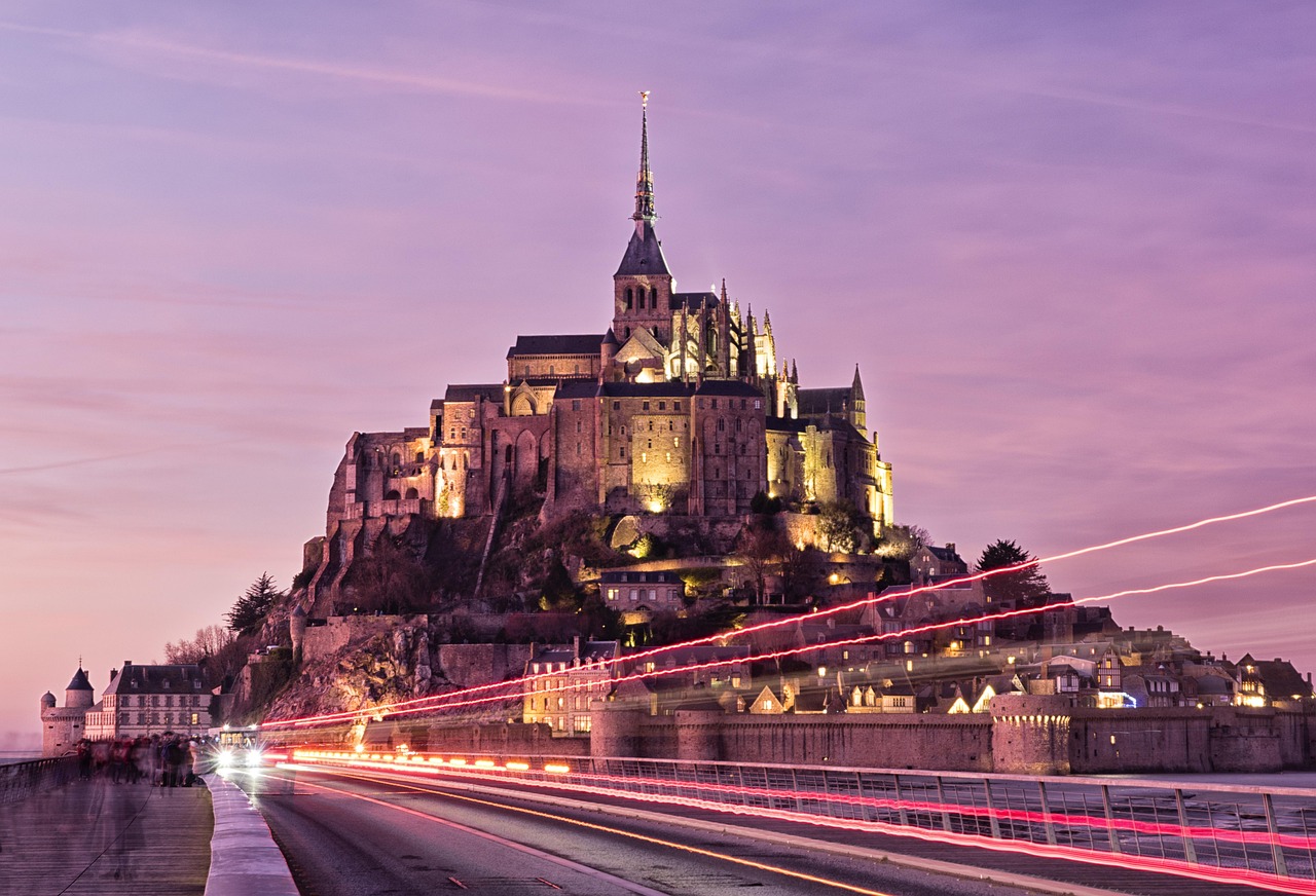 Mont-Saint-Michel floodlit at dusk with light trails on the approach road