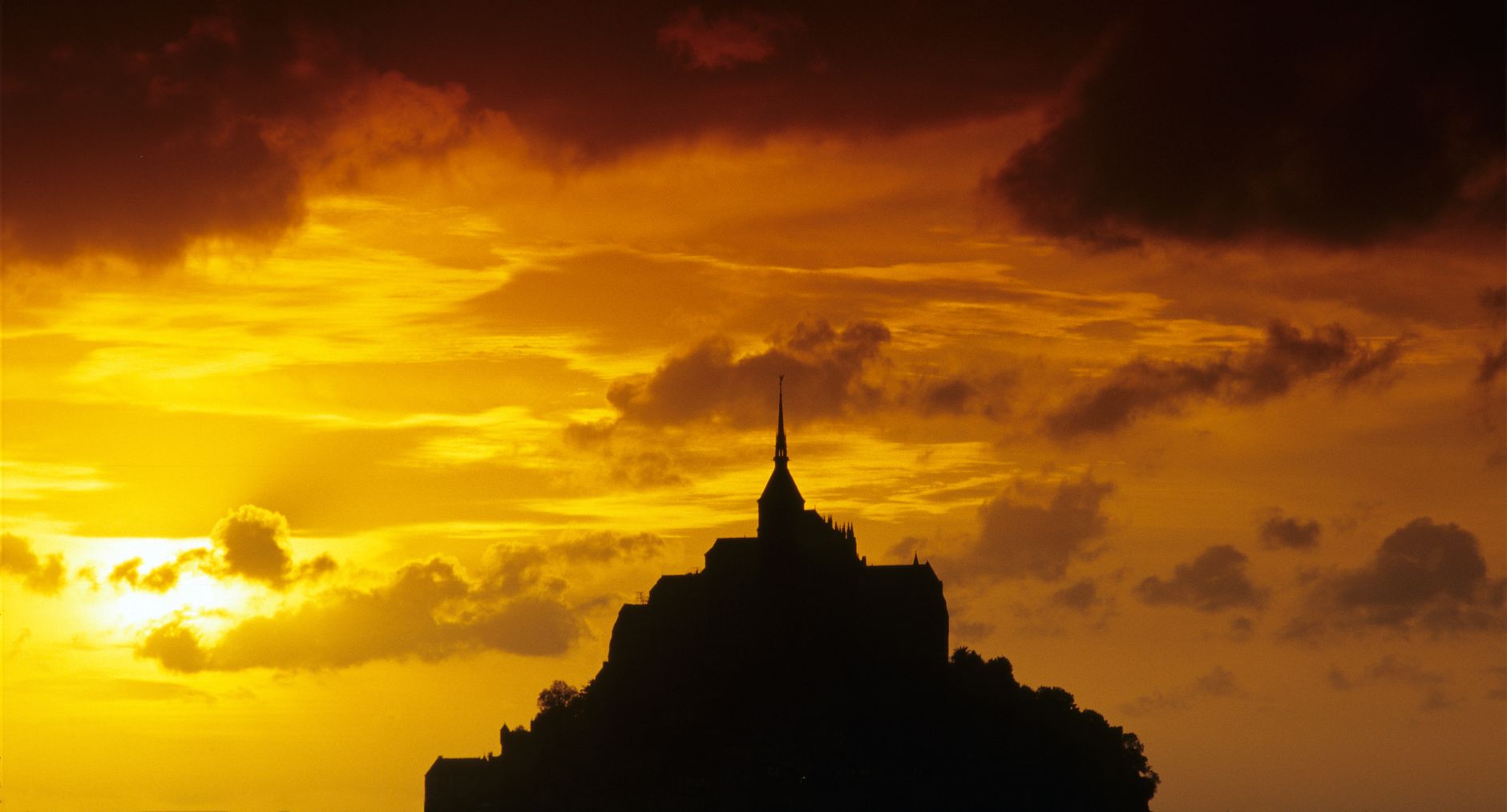 Mont-Saint-Michel in silhouette against an orange and gold sunset sky