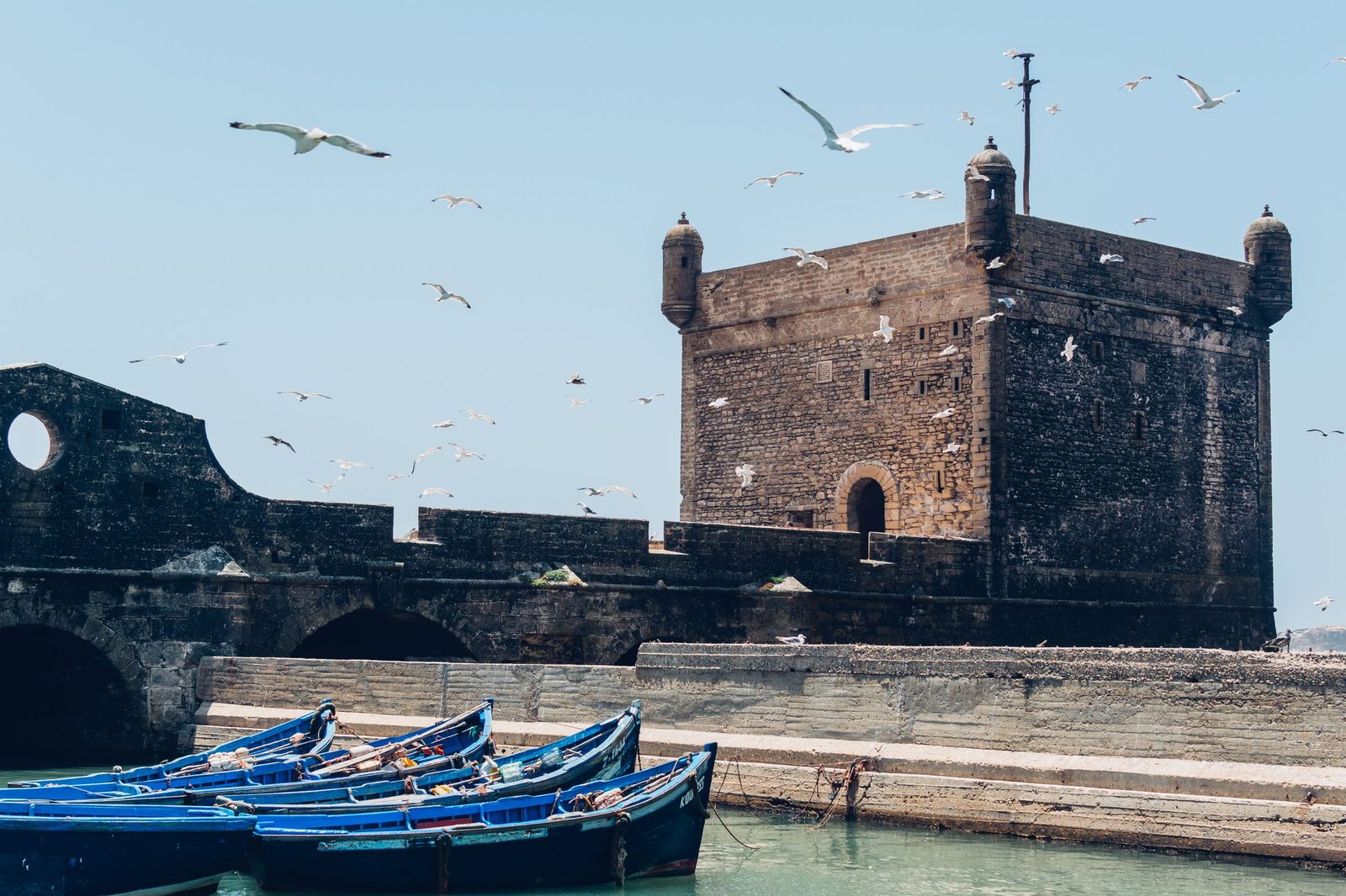 The stone sea bastion of Essaouira with blue fishing boats moored below and gulls in the air