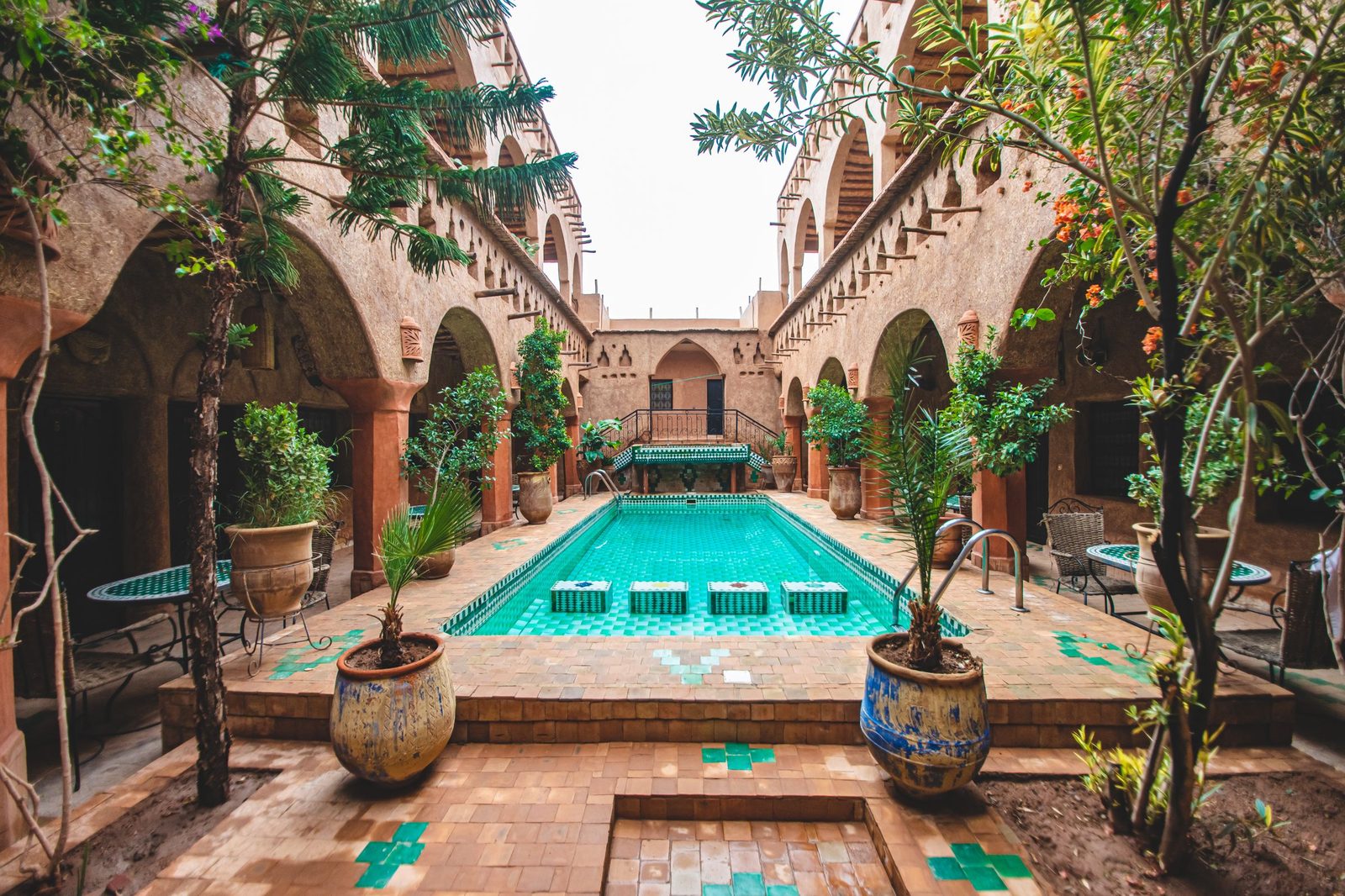 A riad courtyard with a turquoise pool, potted palms and earthen arcades at Aït Benhaddou