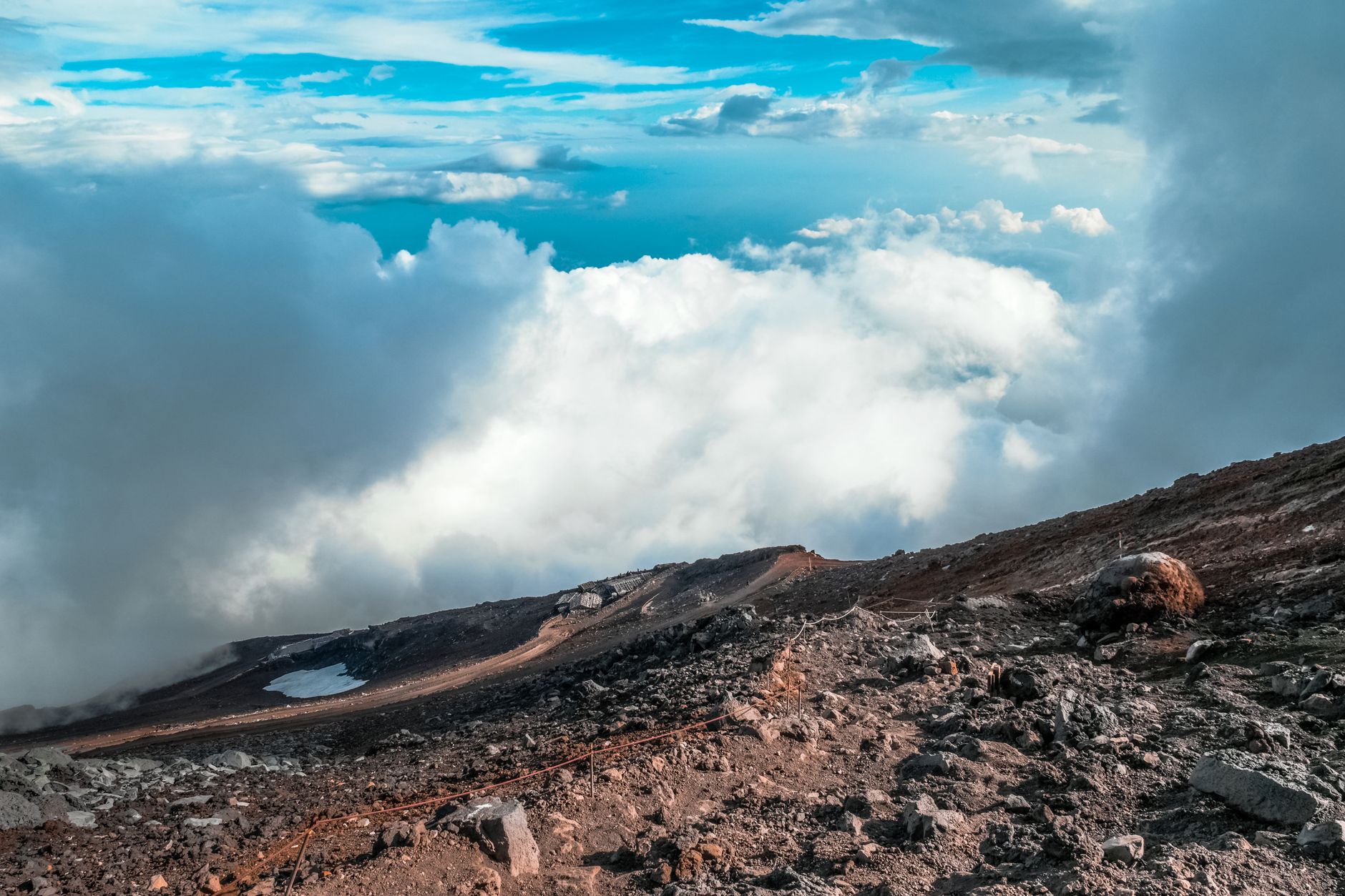 Bare volcanic gravel and rock on Mount Fuji's upper slopes above a bank of cloud