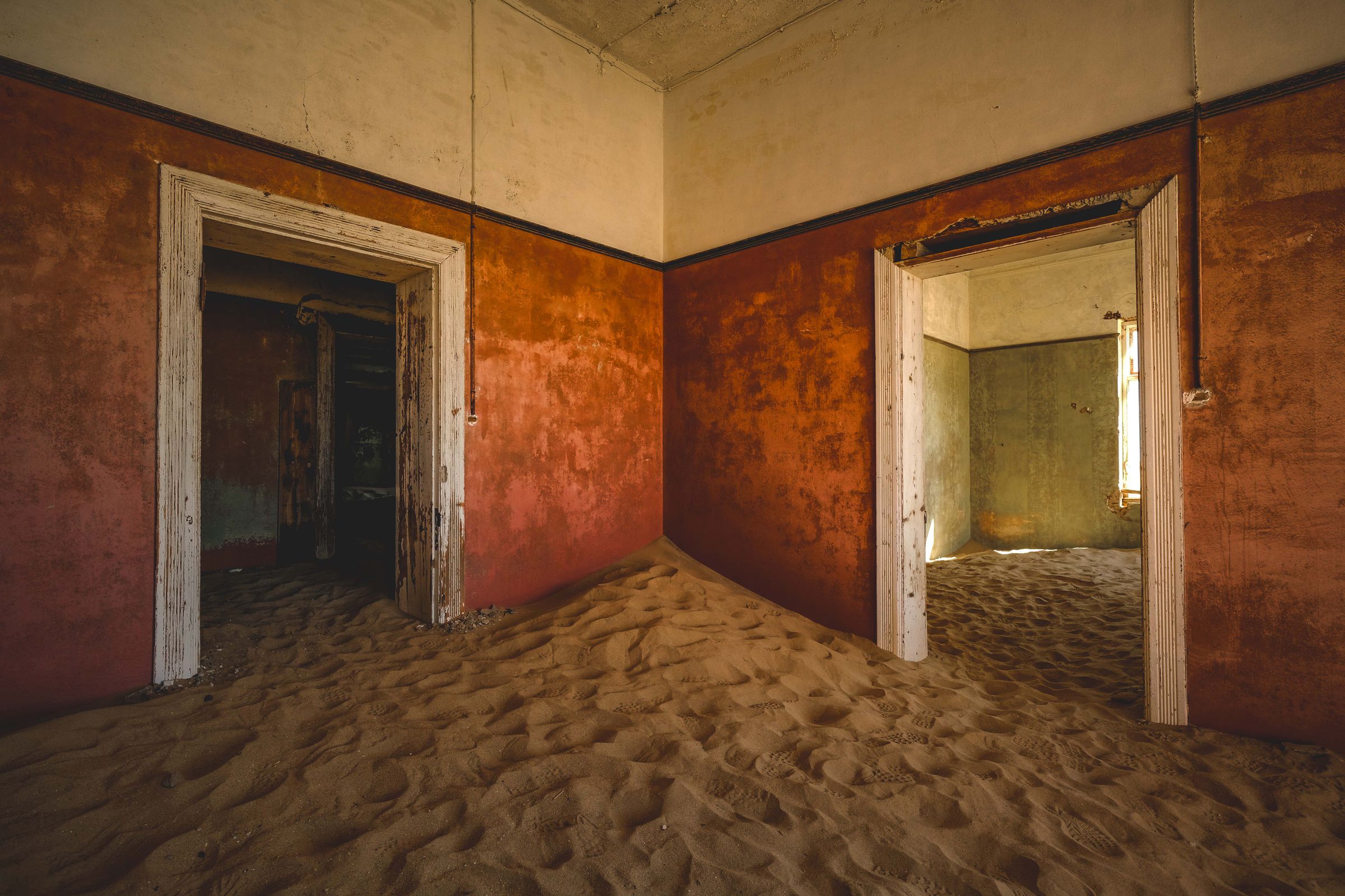 A room at Kolmanskop with burnt orange walls and a dune of sand covering the floor and both doorways