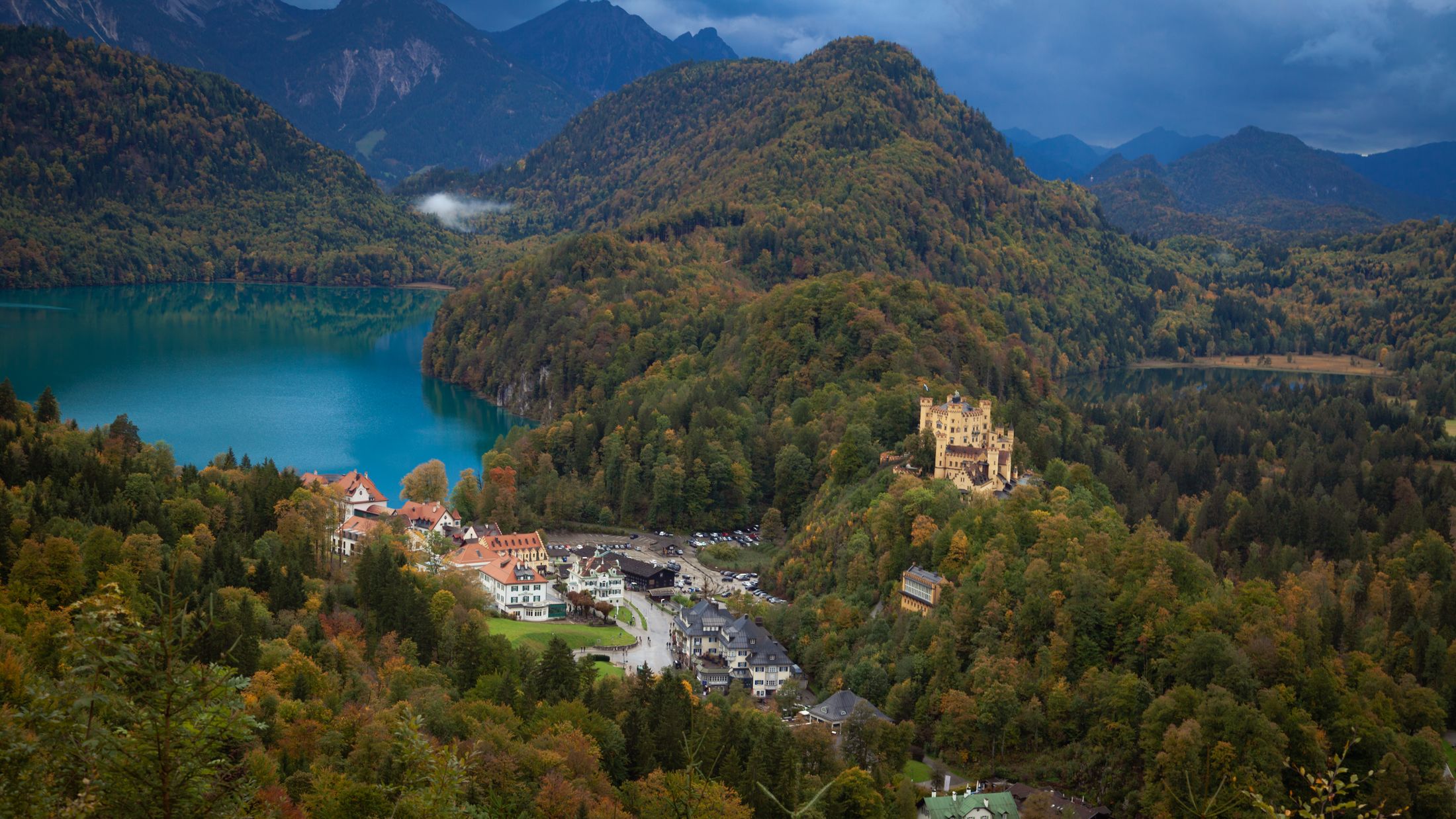 Hohenschwangau castle and village on the turquoise Alpsee lake below Neuschwanstein, autumn forest and the Bavarian Alps behind