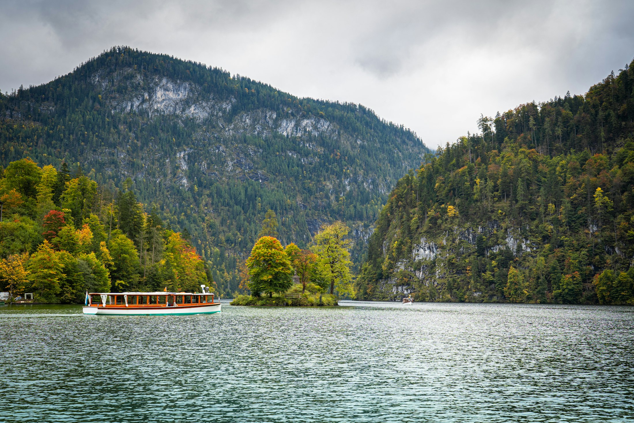 A tour boat on the Alpsee lake below Neuschwanstein, autumn forest and mountains around it
