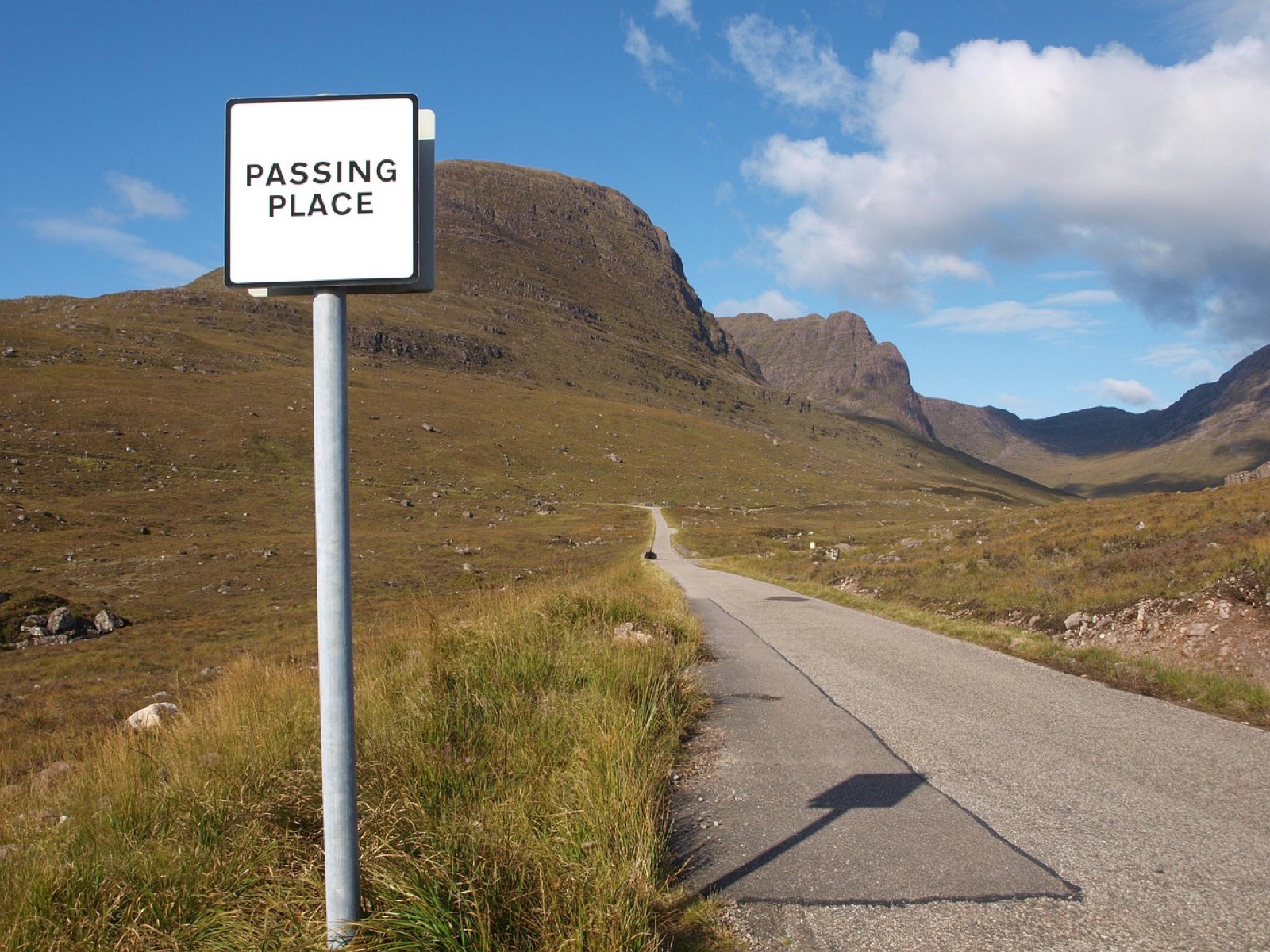 A Passing Place sign beside a narrow road running up a bare mountain pass