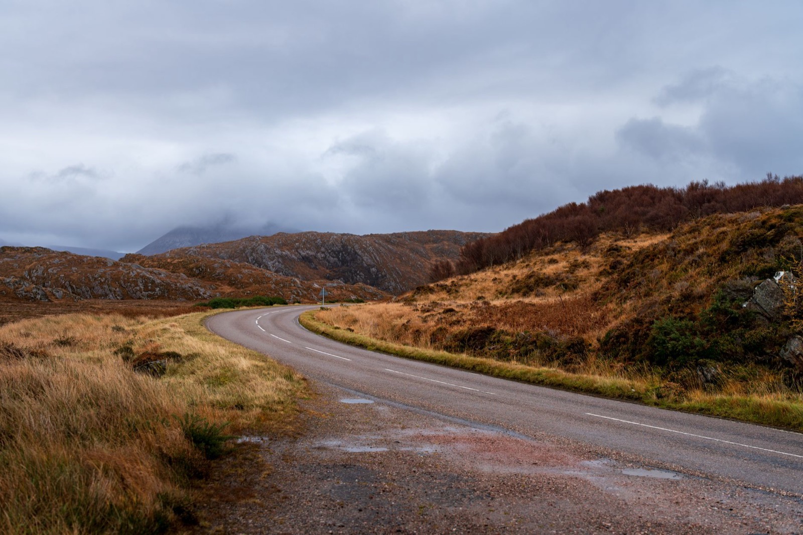 A curving road through rust-coloured moorland and rocky hills under heavy cloud