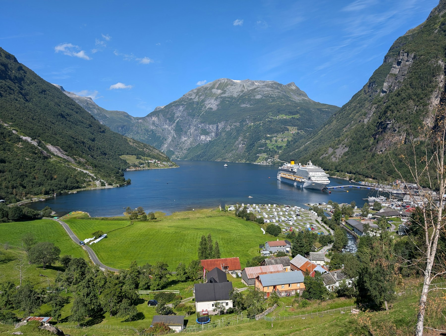 A small fjord village and ferry seen across the water beneath mountains