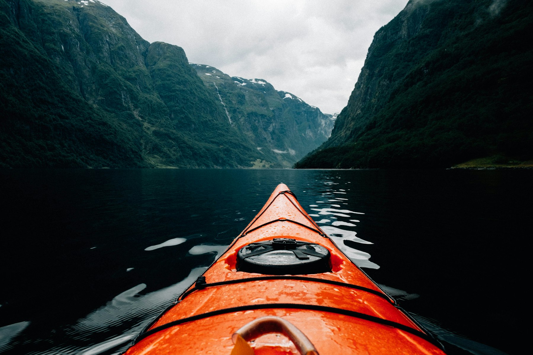 A lone kayak on dark still fjord water dwarfed by steep mountains