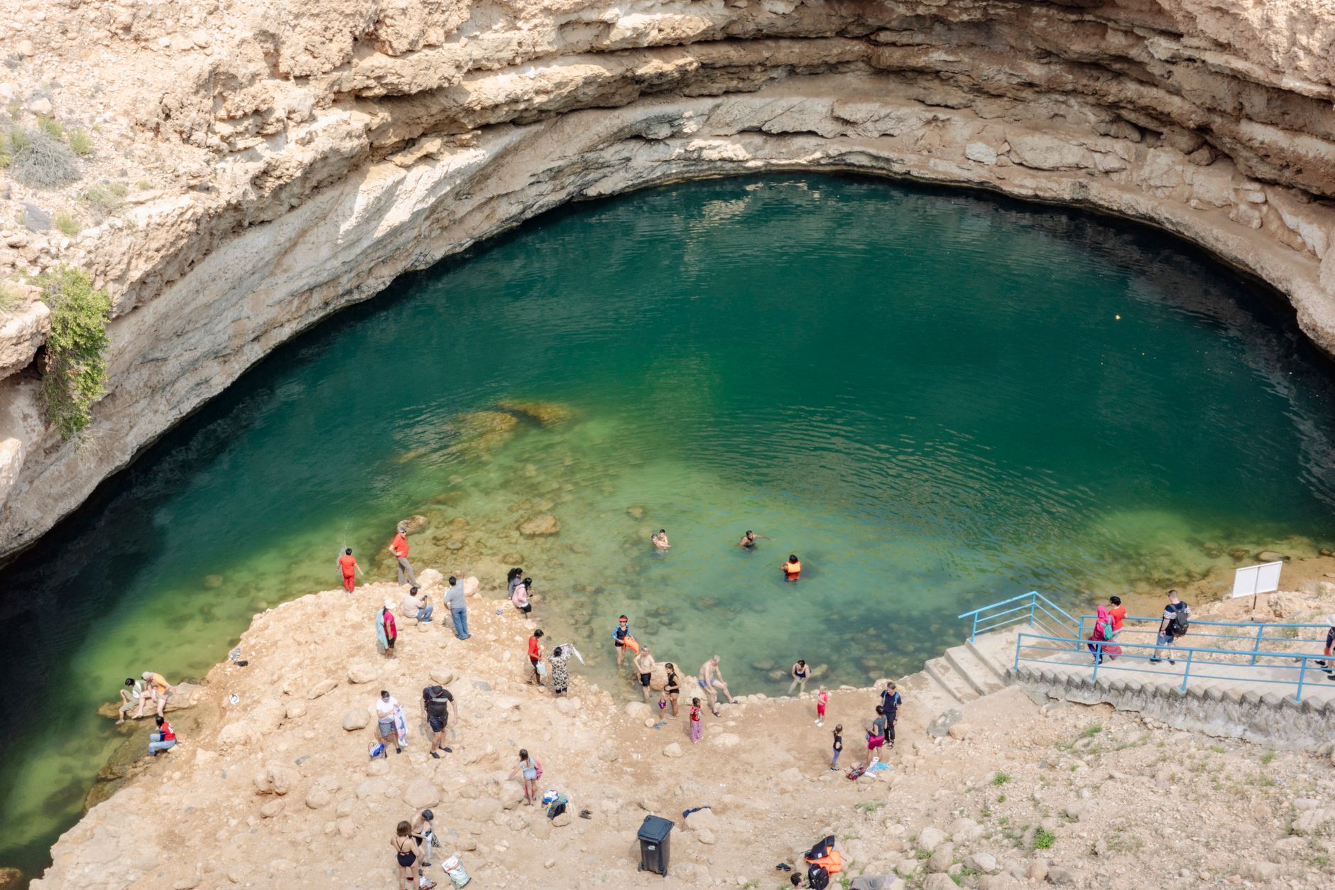 Swimmers in the turquoise Bimmah sinkhole ringed by pale rock