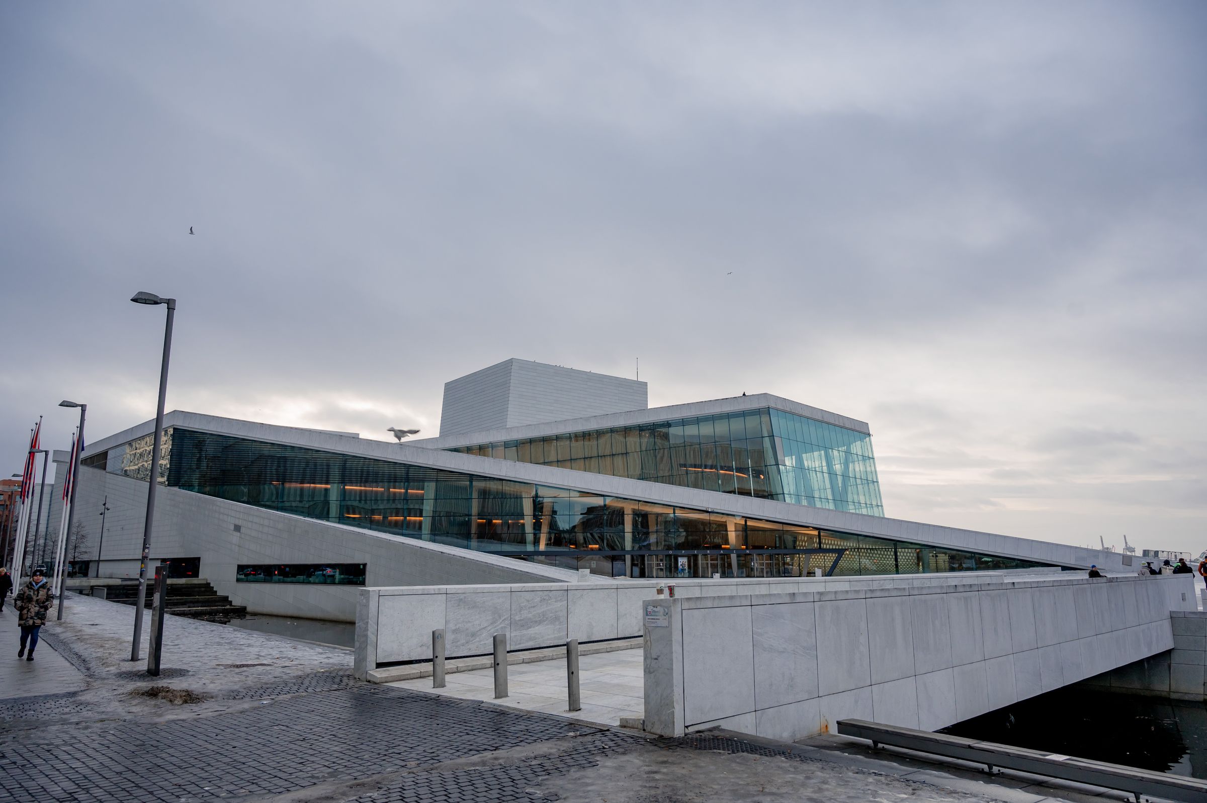 The Oslo Opera House in winter, its white roof sloping down towards the water at the head of the fjord