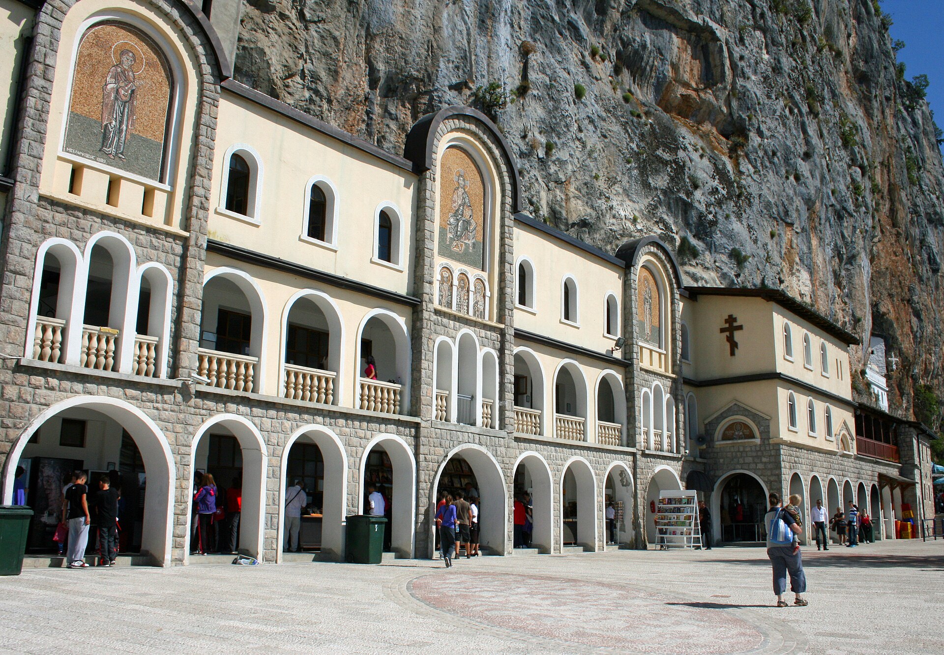 The arcaded white front of the lower monastery at Ostrog with visitors gathered on the paving in front of it
