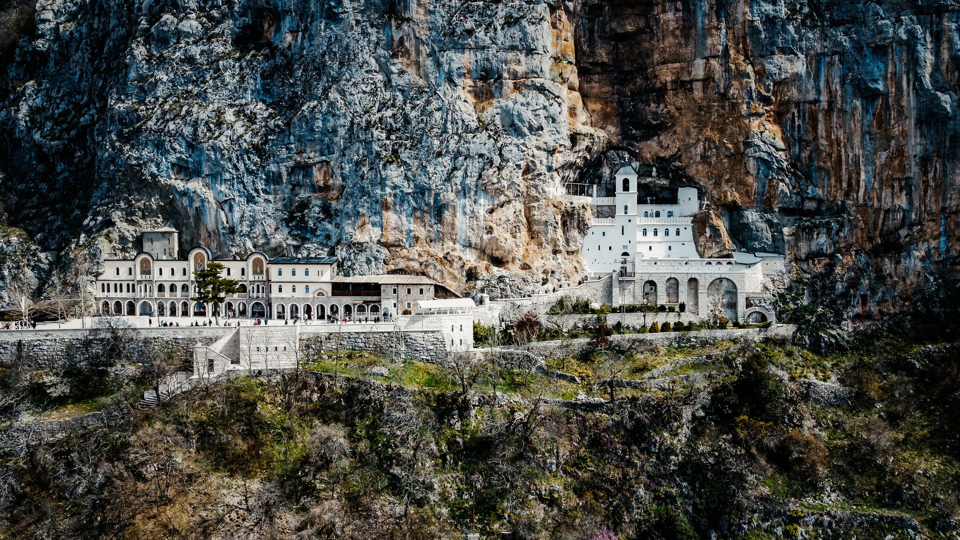 The white monastery of Ostrog small against the full height of the grey limestone cliff it is built into