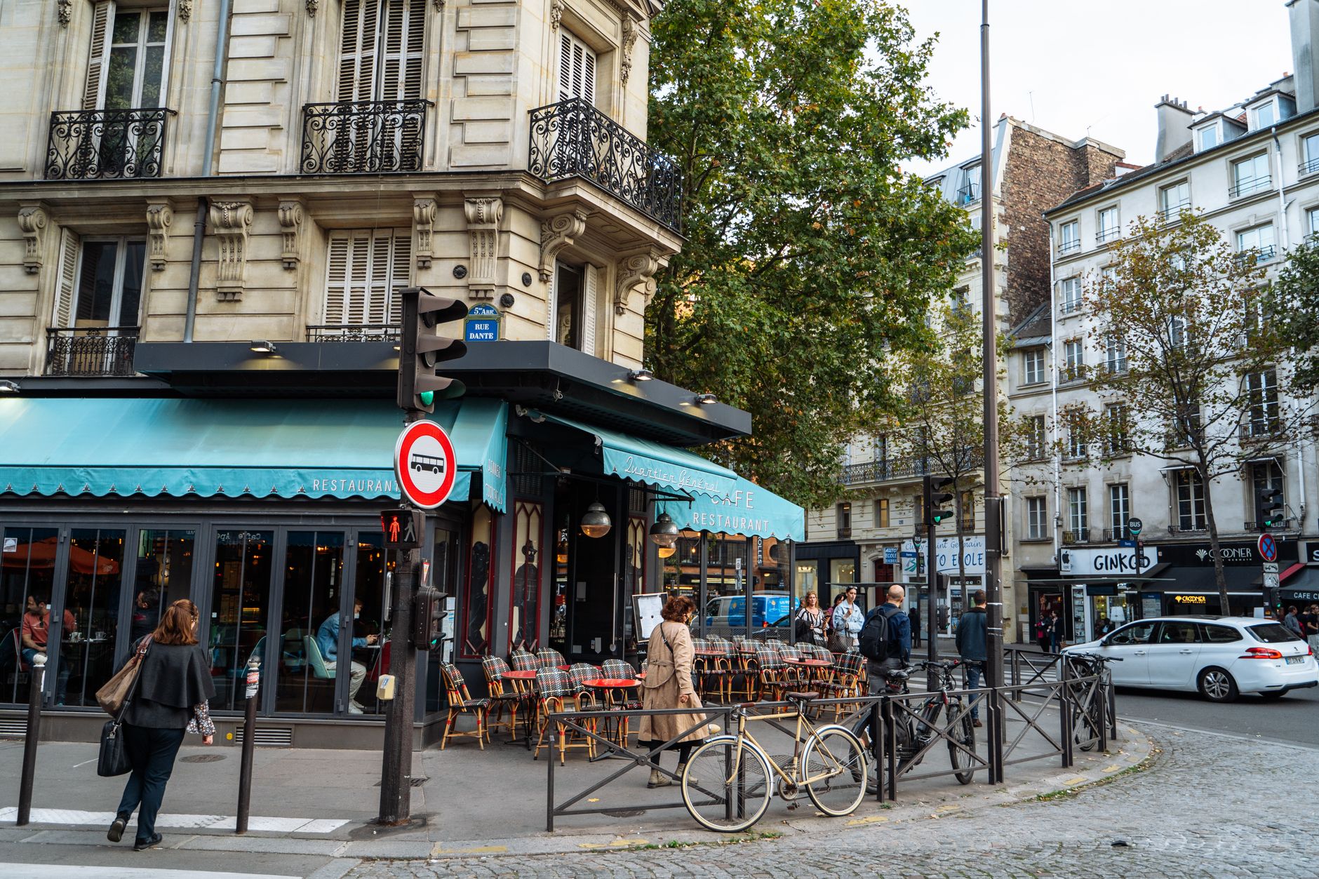 A classic Paris corner cafe with a teal awning and cane chairs on the pavement