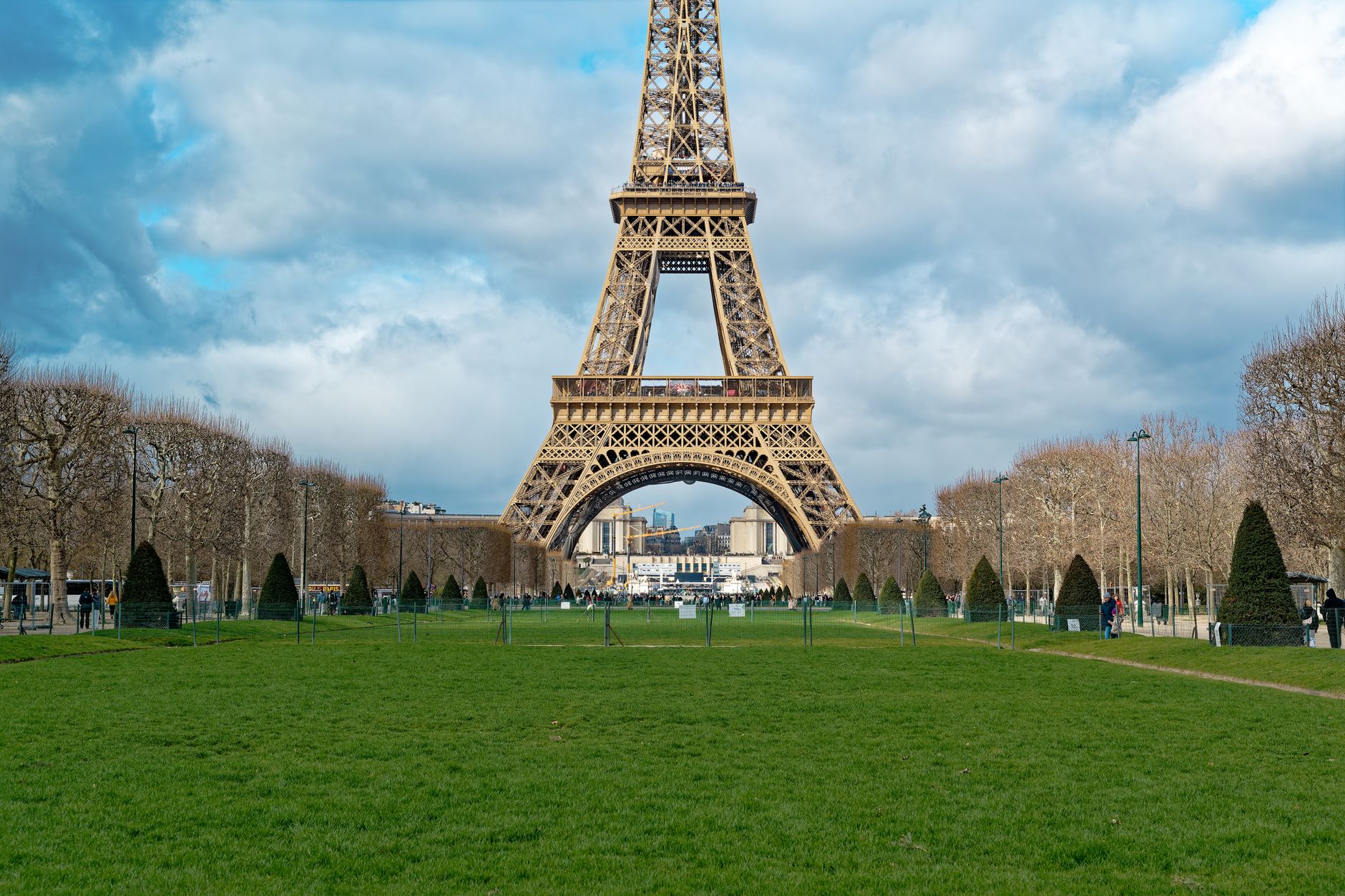 The Eiffel Tower lit at dusk seen from the lawns of the Champ de Mars, people sitting on the grass