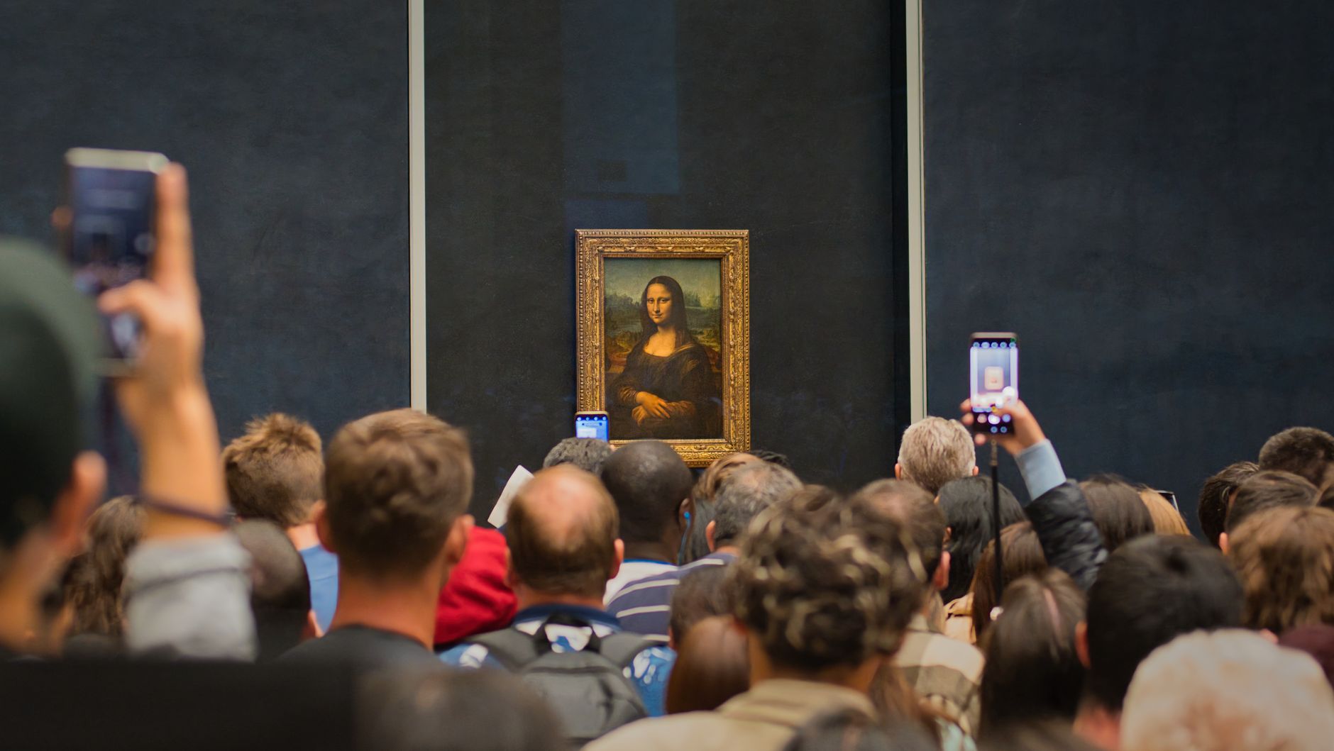 Visitors photographing the Mona Lisa behind glass in a crowded gallery at the Louvre