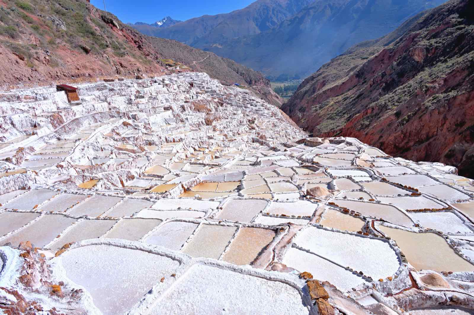 The white salt pans of Maras stepping down a red mountainside towards the Sacred Valley, with a snow peak on the skyline