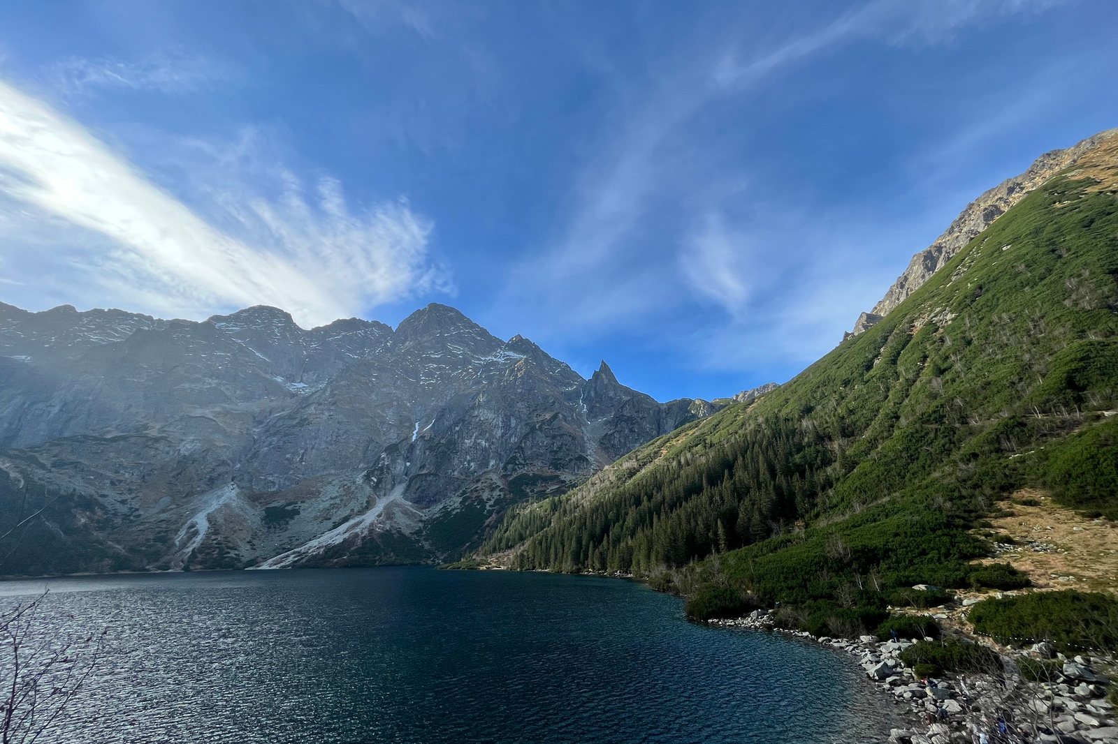 Morskie Oko, a dark mountain lake below the granite walls of the High Tatras, with a forested slope on the right