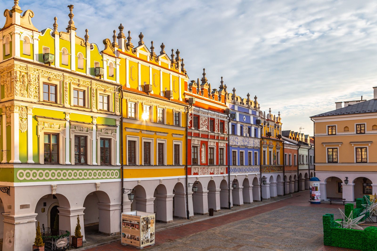 Renaissance merchant houses painted yellow, red and blue around the market square of Zamość, with arcades at street level