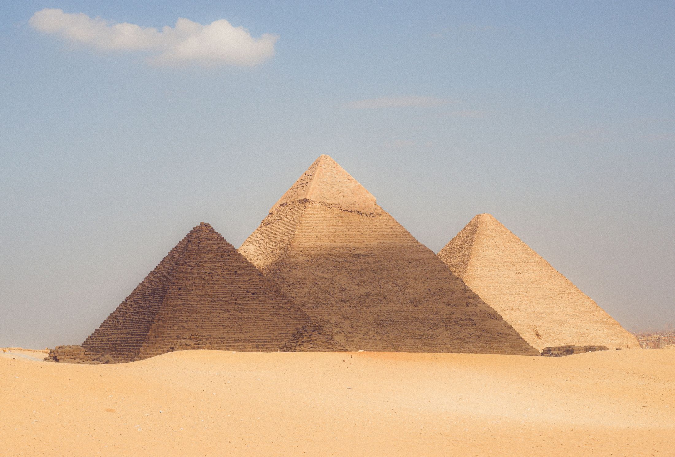 The three Pyramids of Giza lined up in golden desert sand under a clear sky