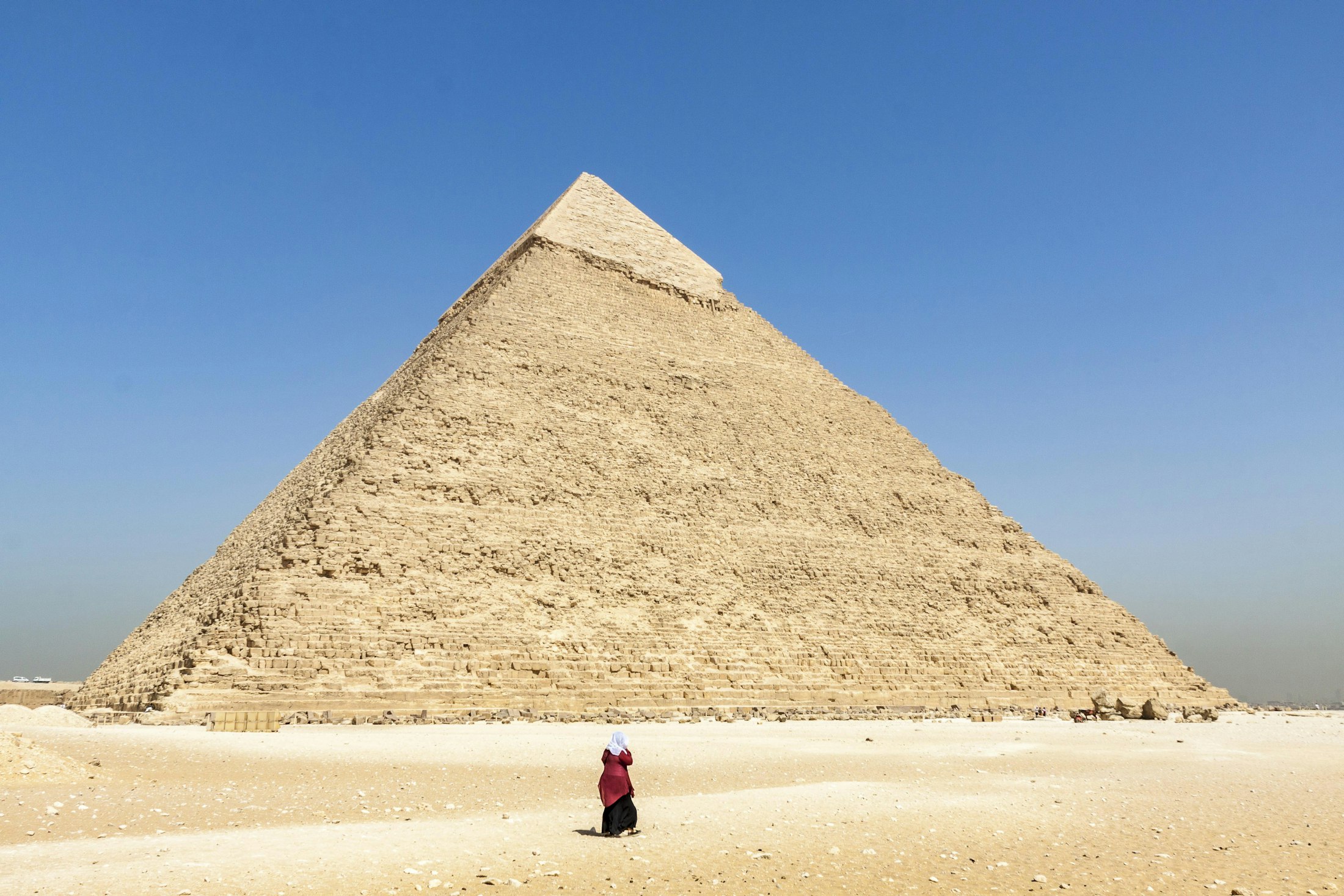 A single tiny figure standing at the base of the vast Pyramid of Khafre at Giza, giving a sense of its scale