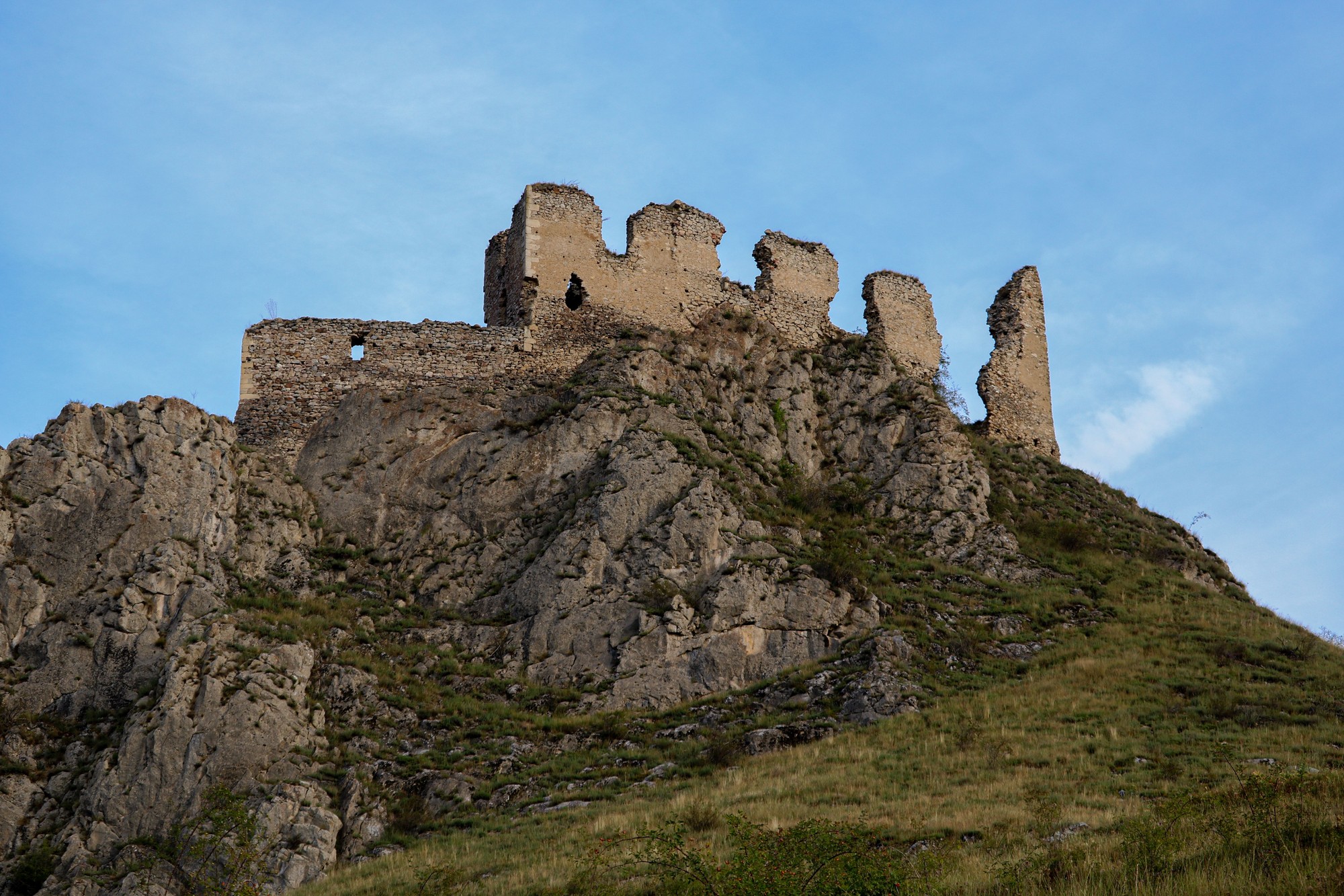The broken towers and walls of a medieval castle standing on a rocky outcrop above grass