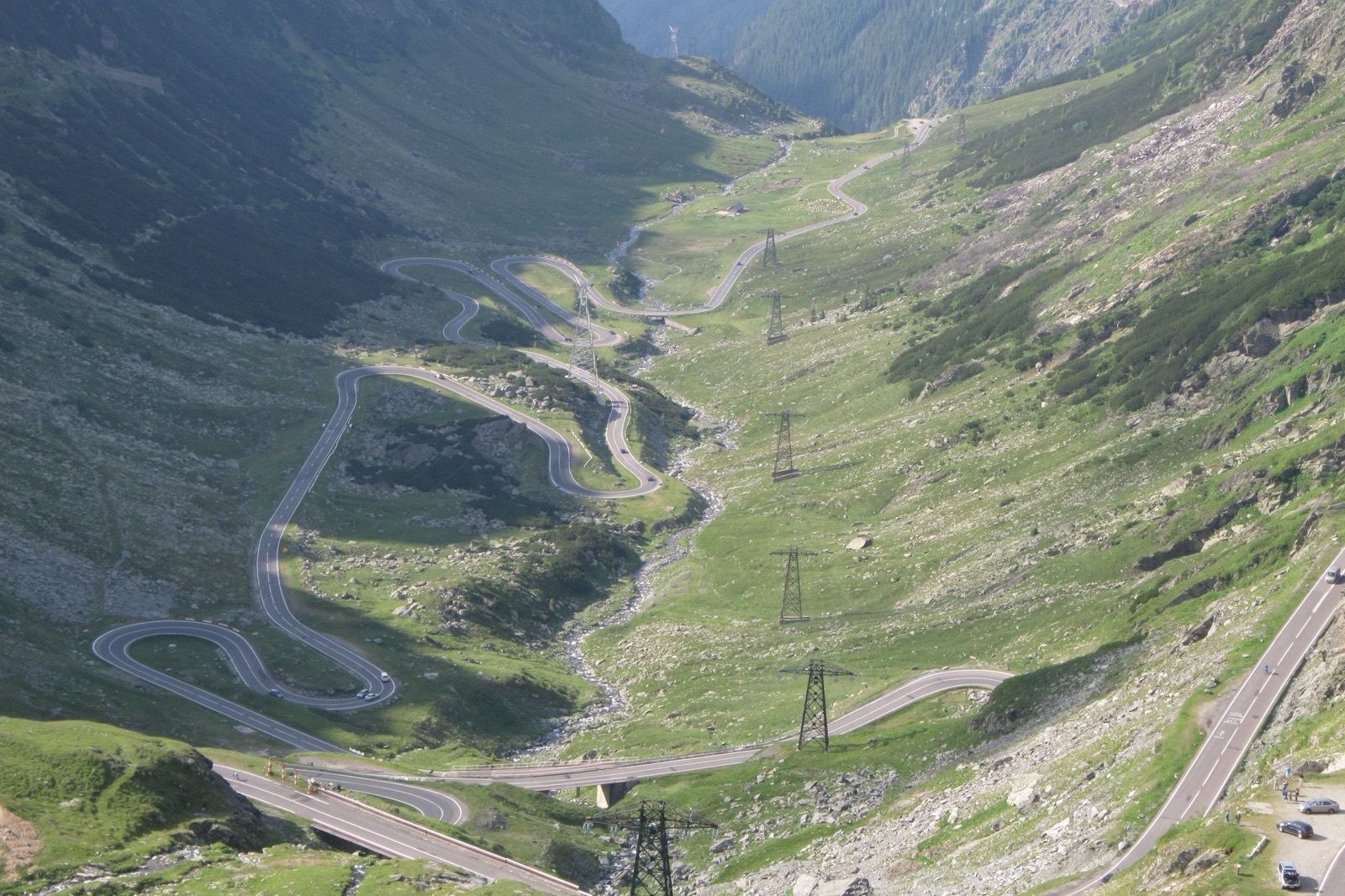 The Transfăgărășan road climbing the north side of the Făgăraș mountains in tight hairpins, pylons along the green valley floor
