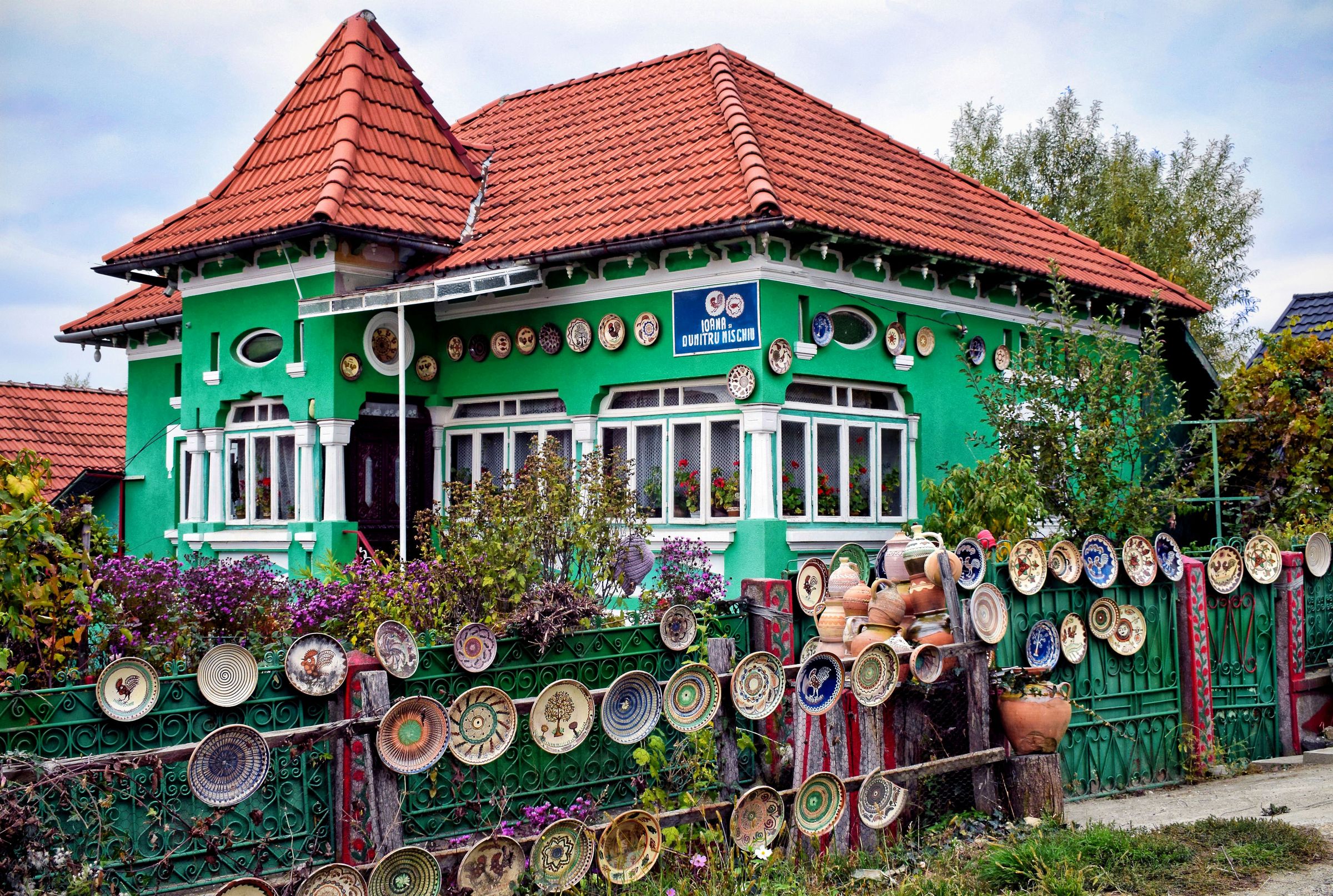 A green village house at Rămești with painted Horezu plates hung along its fence and under its eaves