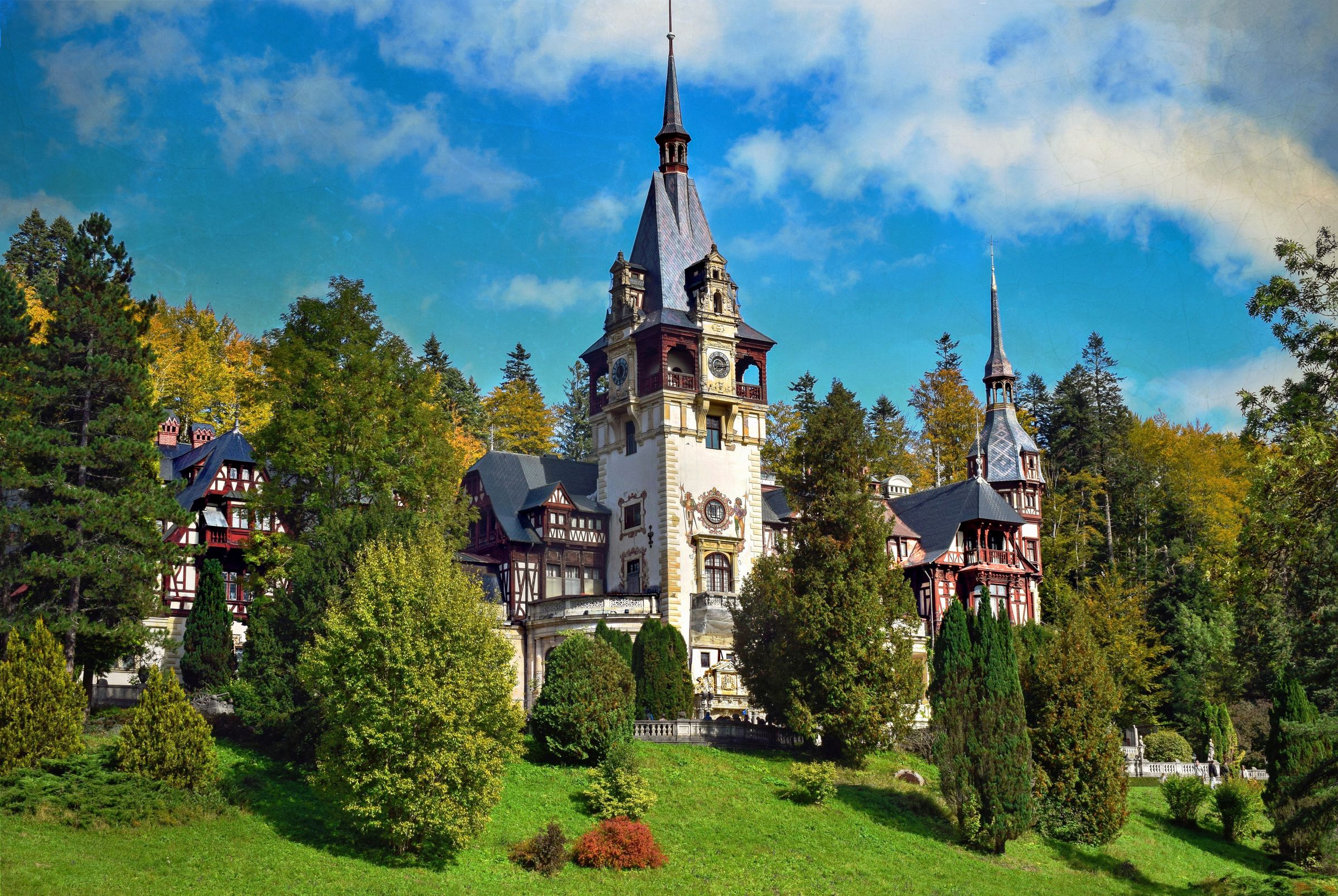 Peleș Castle among autumn trees at Sinaia, its clock tower and timbered gables rising over the terraces