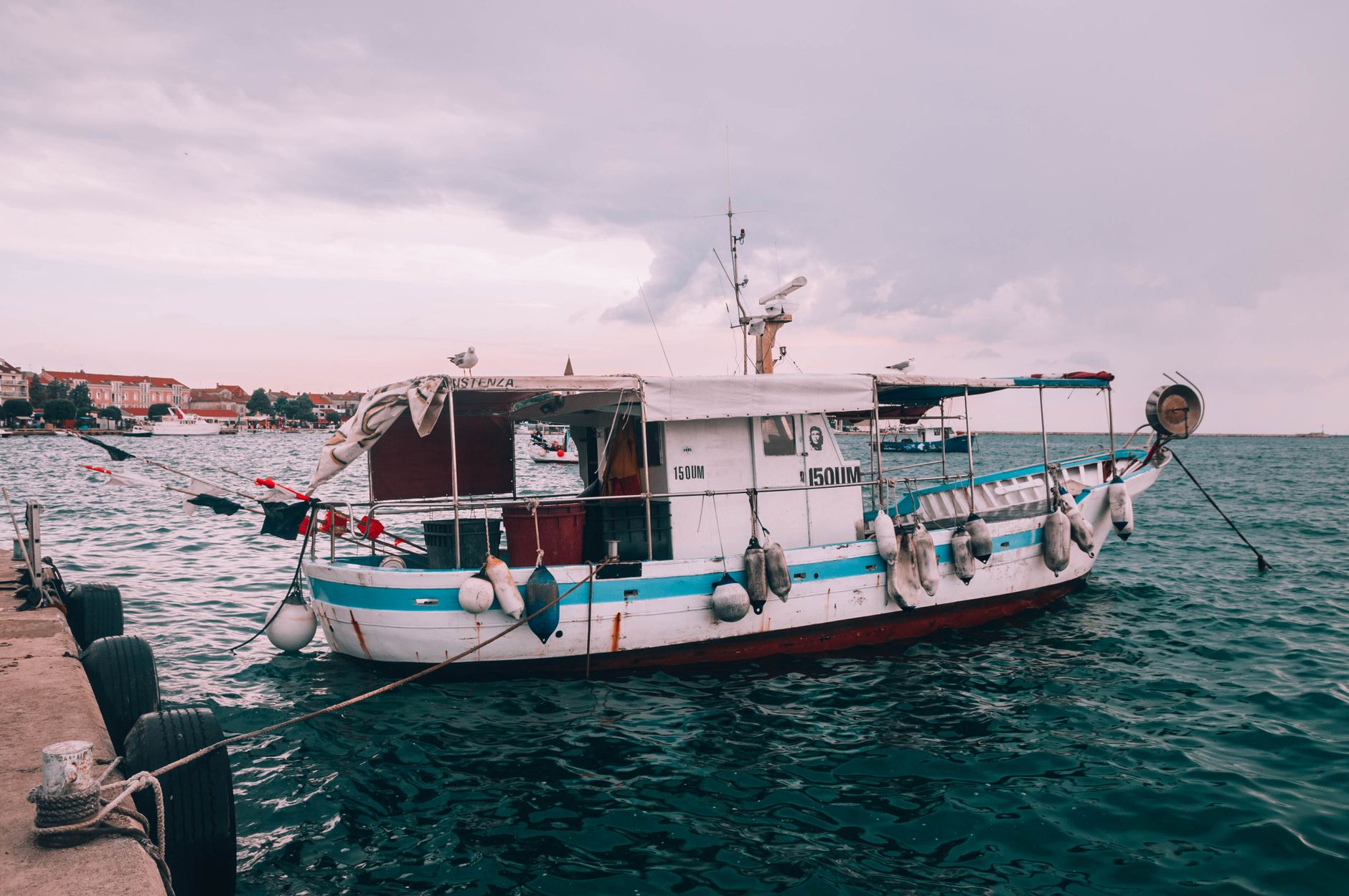 A wooden fishing boat with a small wheelhouse riding at anchor on open water