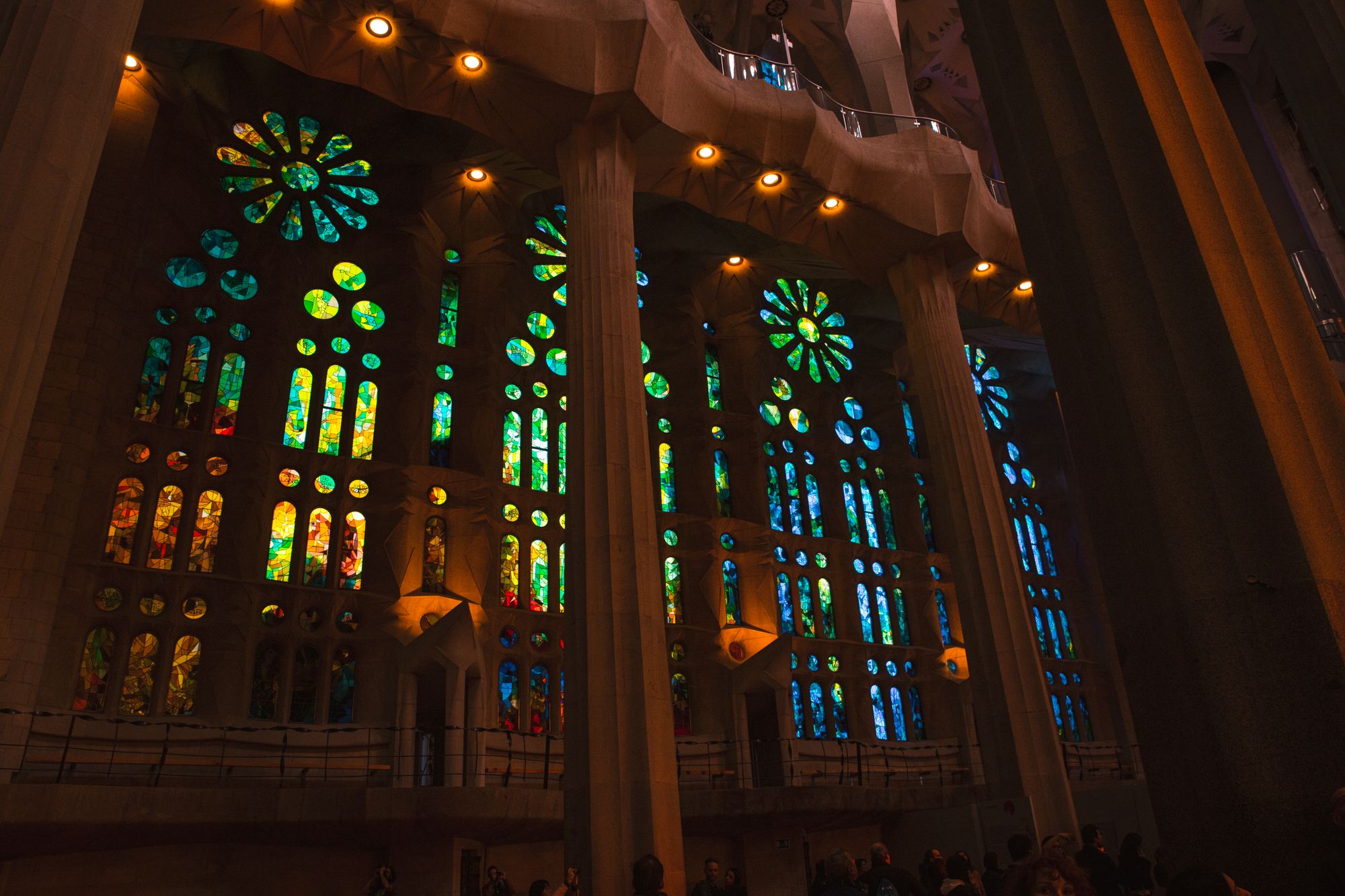 Blue and green stained glass windows on the eastern Nativity side of the Sagrada Família, casting cool morning light