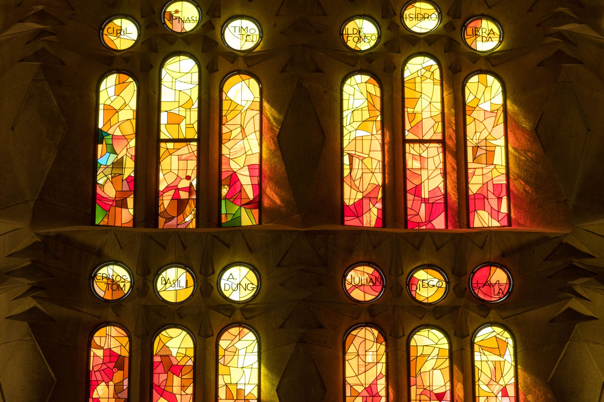 Red and amber stained glass windows on the western Passion side of the Sagrada Família, casting warm evening light