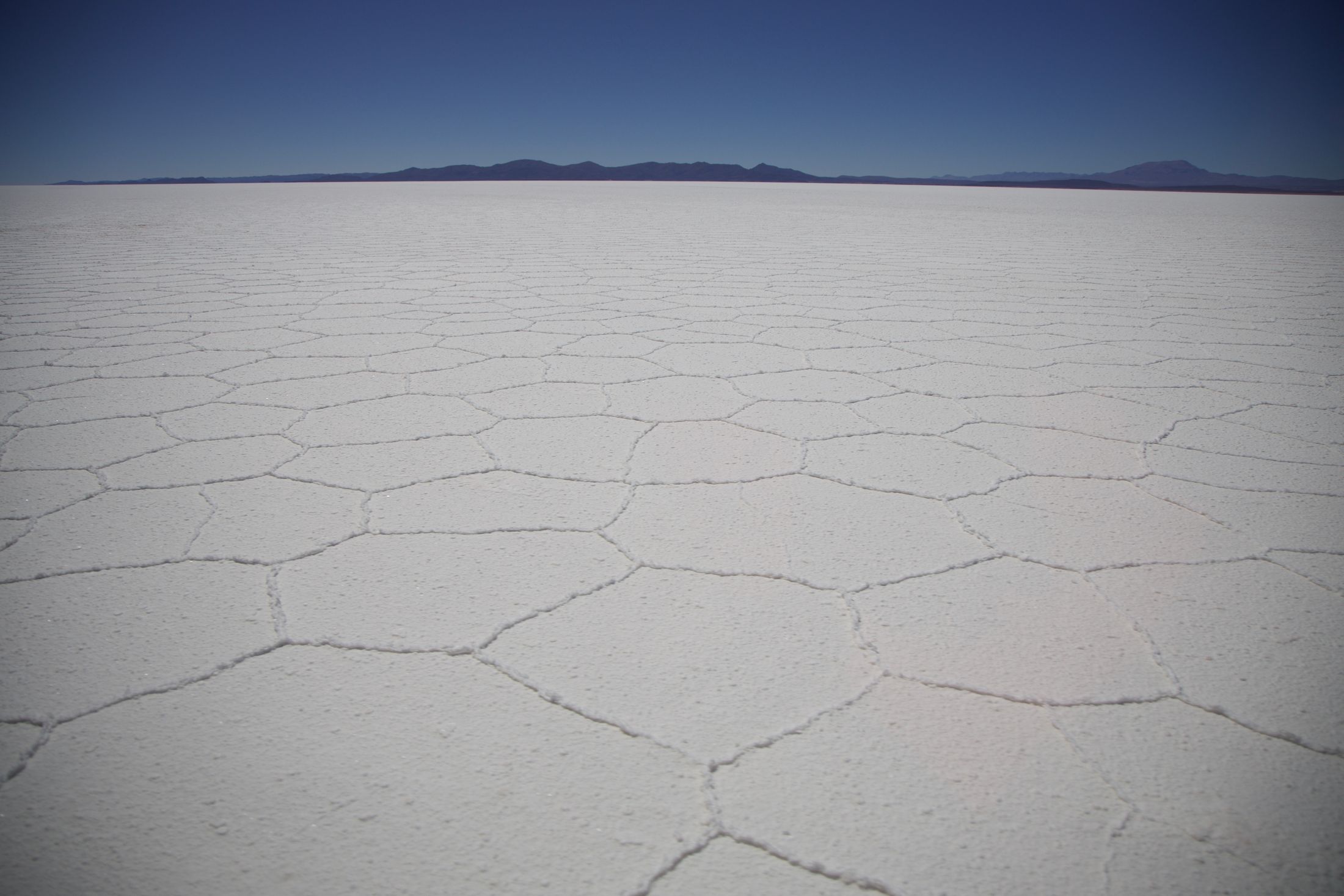 The white hexagonal salt tiles of the dry Salar de Uyuni stretching to distant mountains