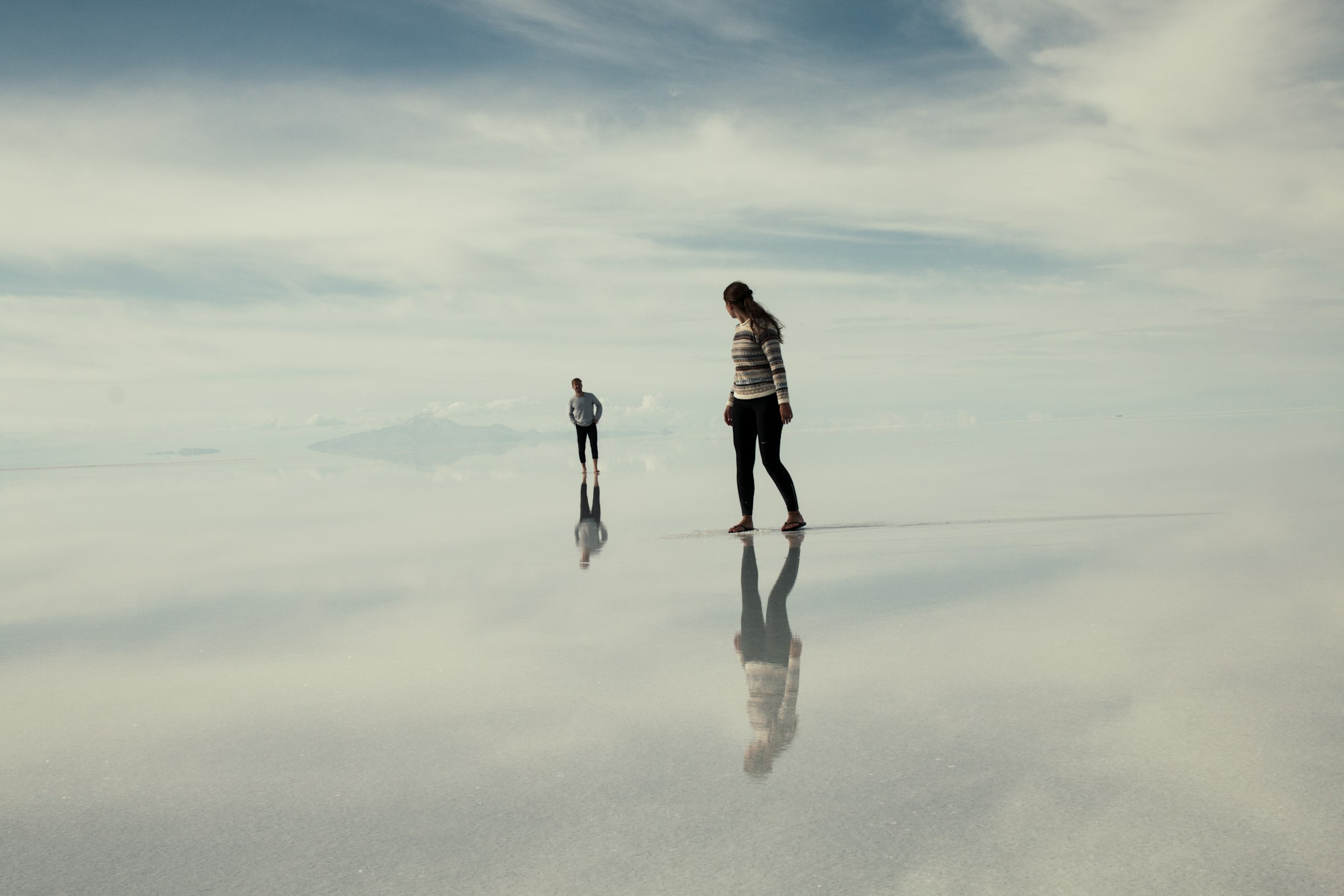 Two people appearing to walk on the sky as clouds reflect in the flooded mirror of Salar de Uyuni
