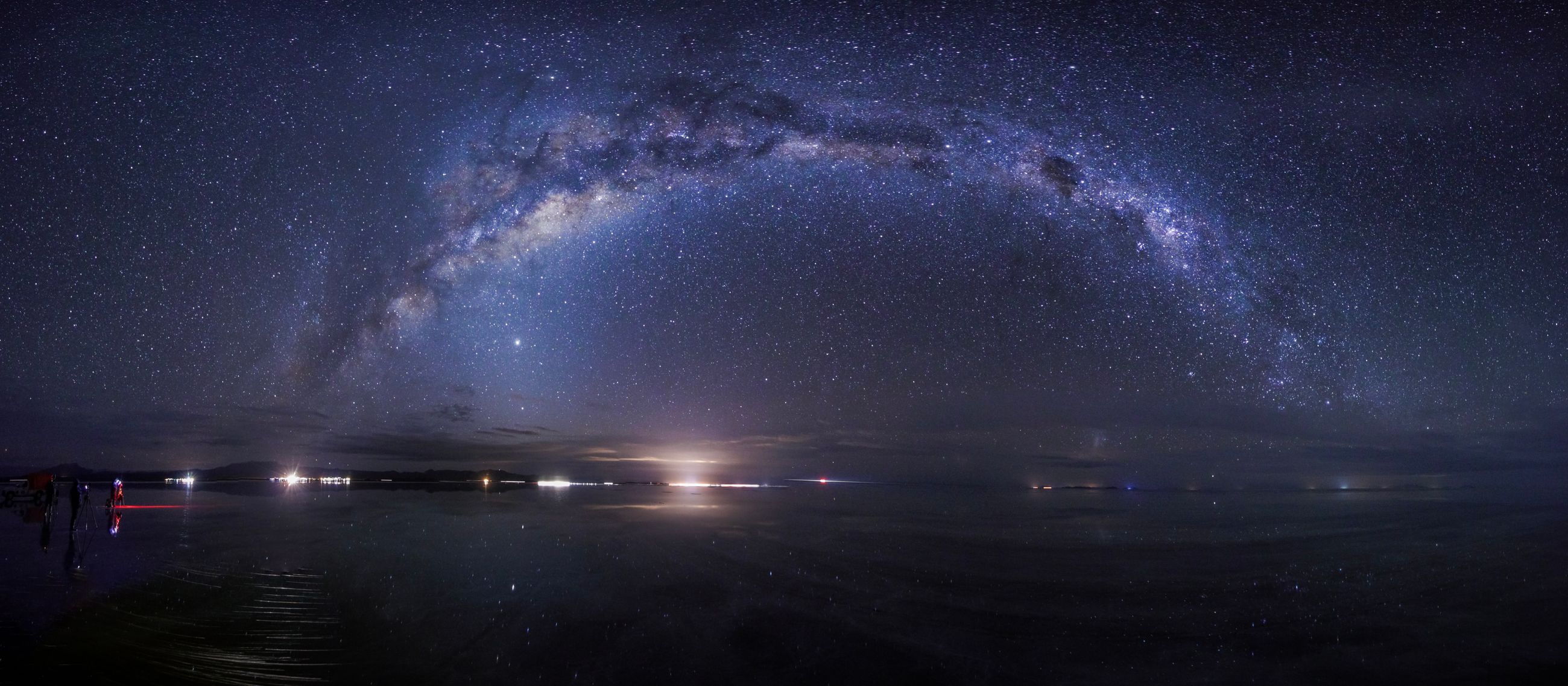 The arc of the Milky Way over the Salar de Uyuni at night, faintly mirrored in the water below