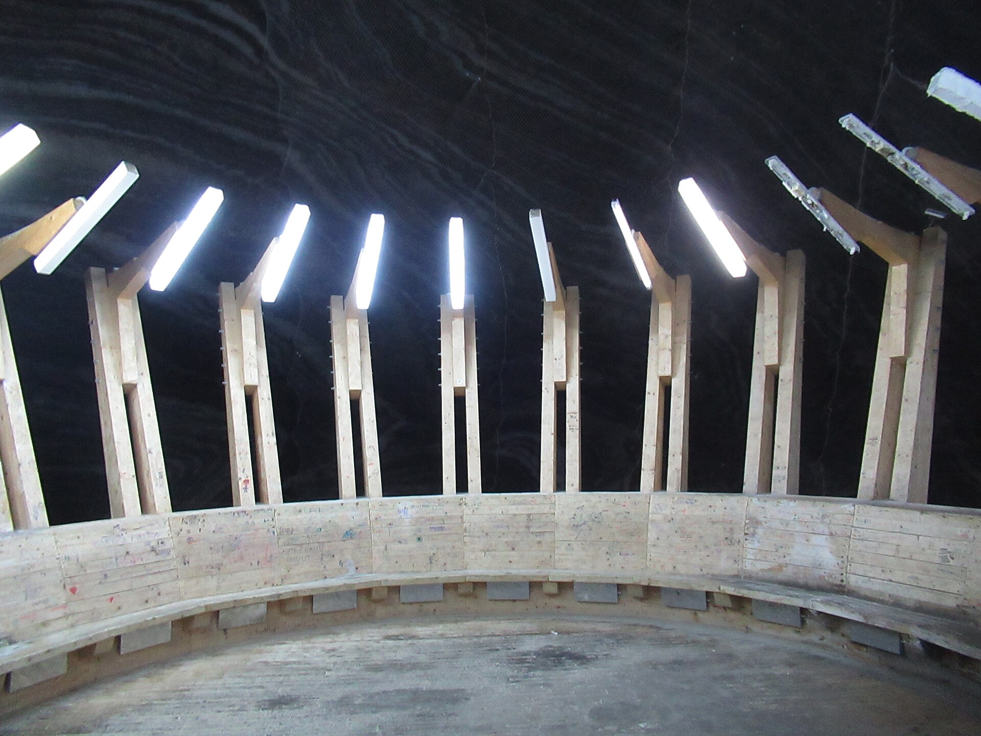 A curved timber bench and raking lights built against a black salt wall