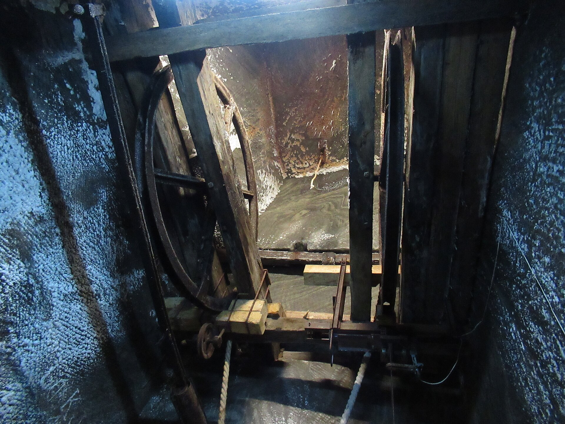A large wooden wheel and timber frame standing in a salt-crusted shaft