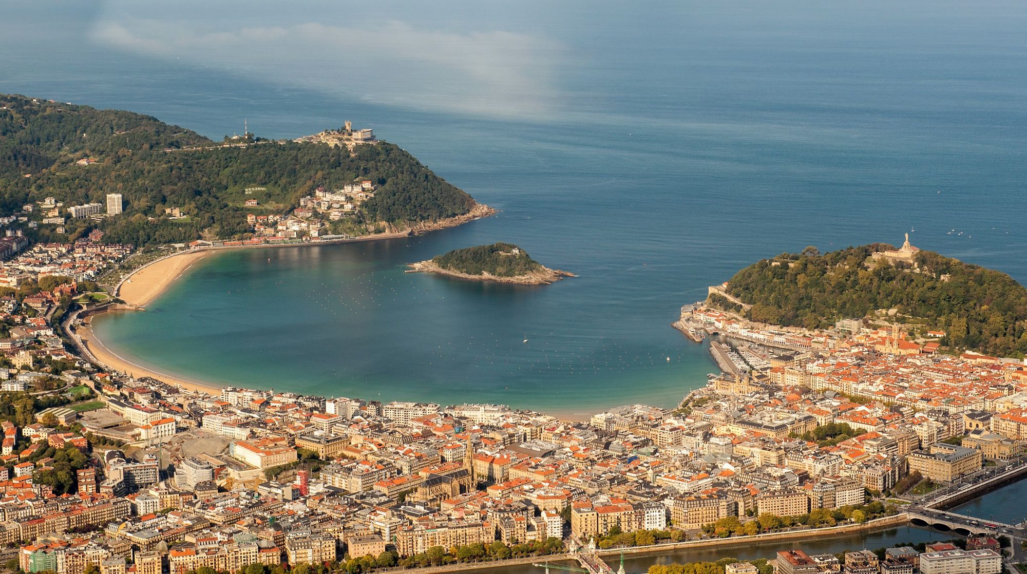 San Sebastián from the air, La Concha beach curving round the bay between Monte Igueldo and Monte Urgull, with Santa Clara island in the middle