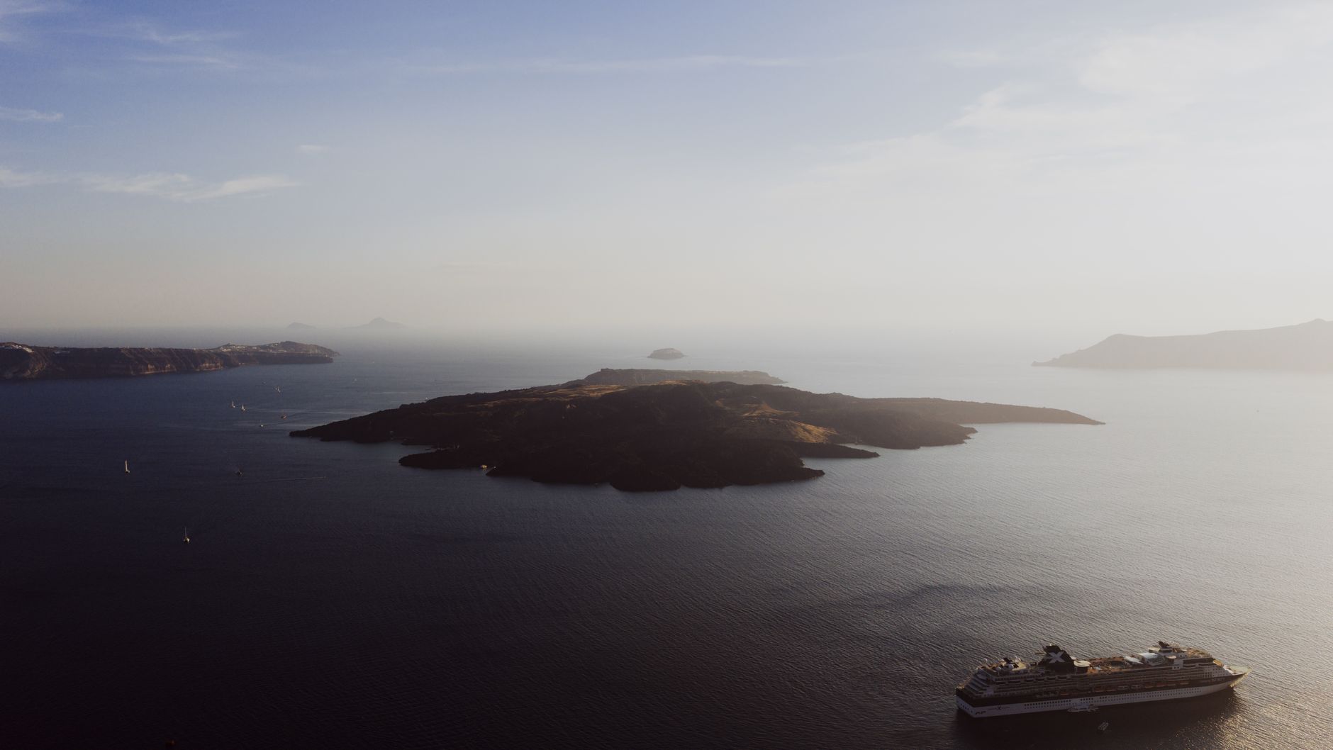 A small boat on the dark caldera water beside the low black volcanic island of Nea Kameni, Santorini