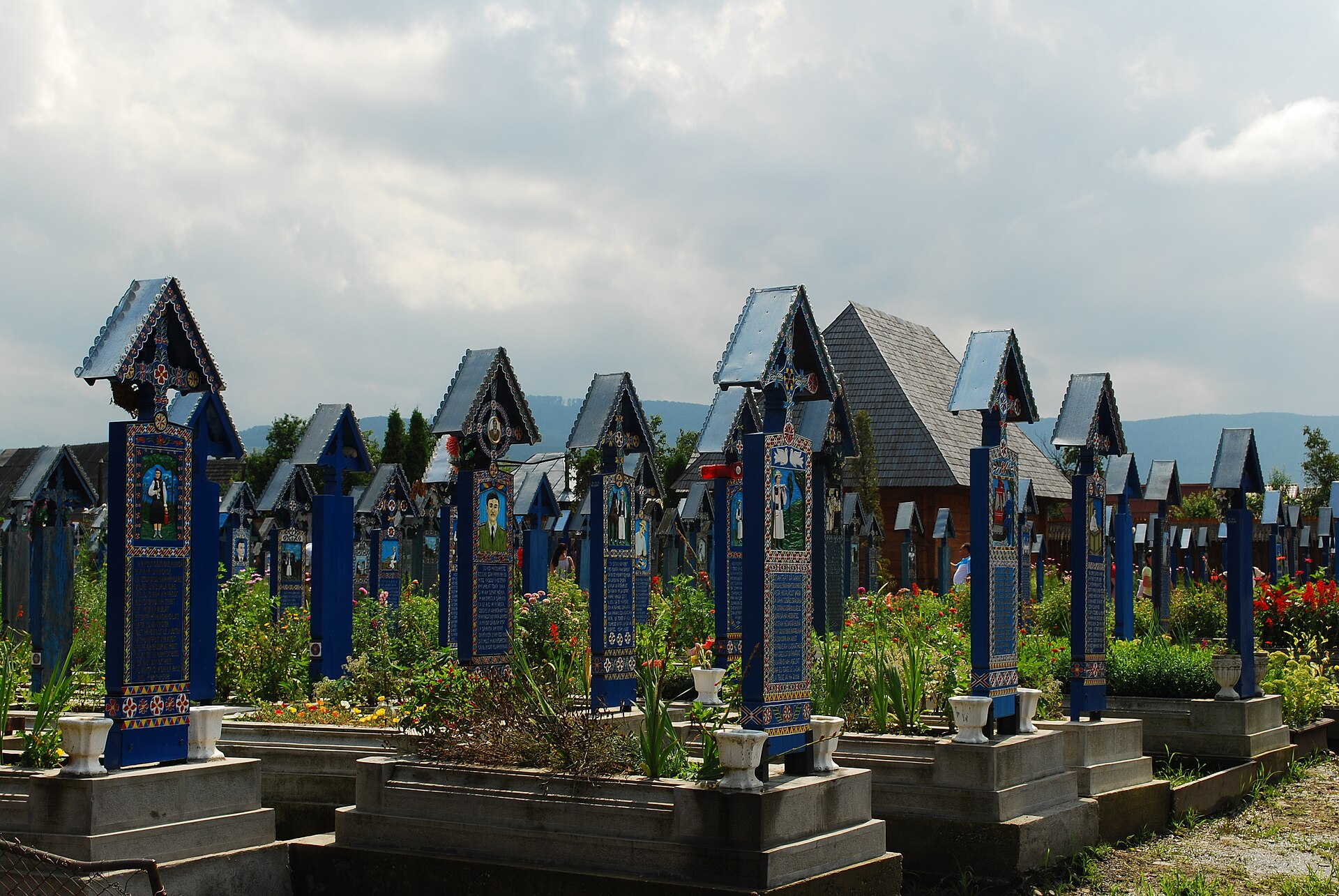 Rows of blue painted wooden crosses with the shingled church roof and hills behind