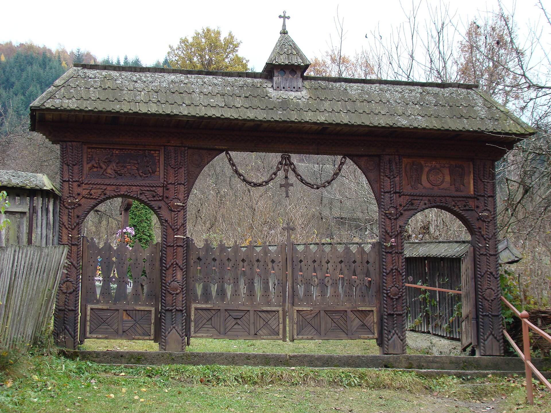 A large carved oak gate under a shingled roof, with rope patterns and rosettes cut into the posts