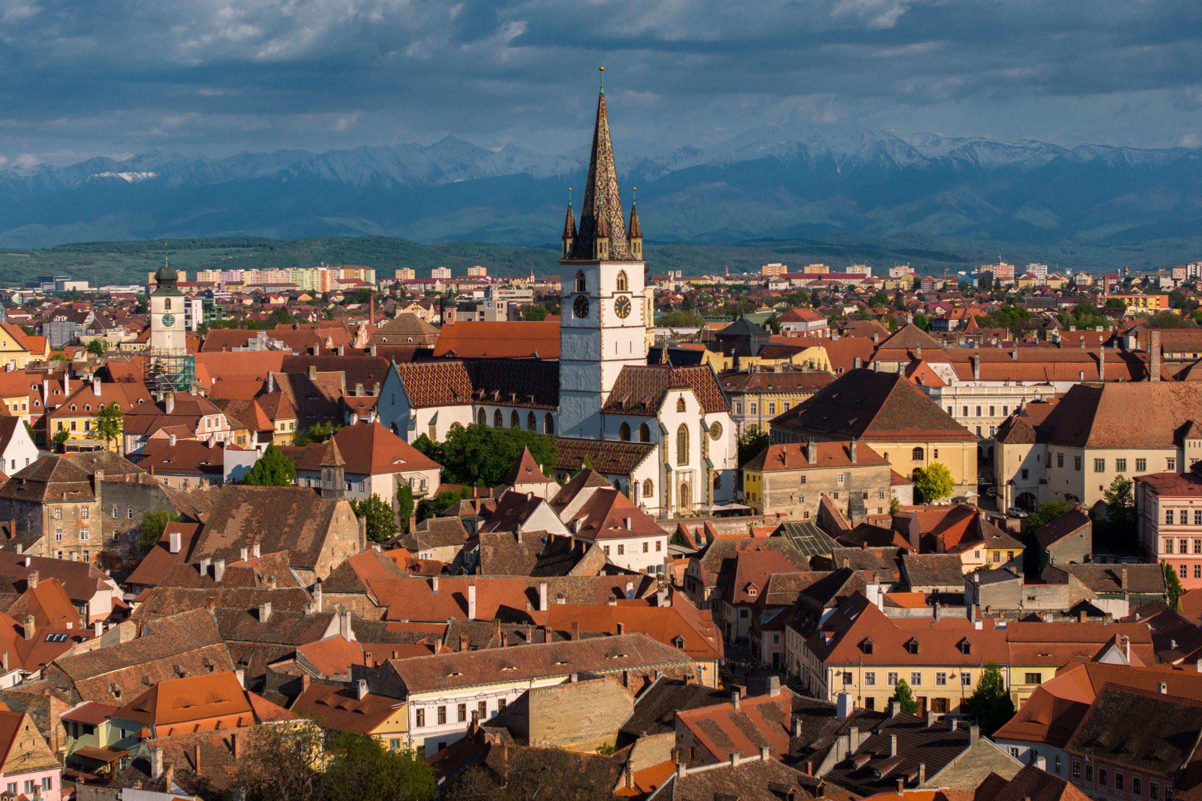 Sibiu's upper town looking south, the Lutheran cathedral spire above red roofs, the Council Tower to its left and snow on the mountains behind