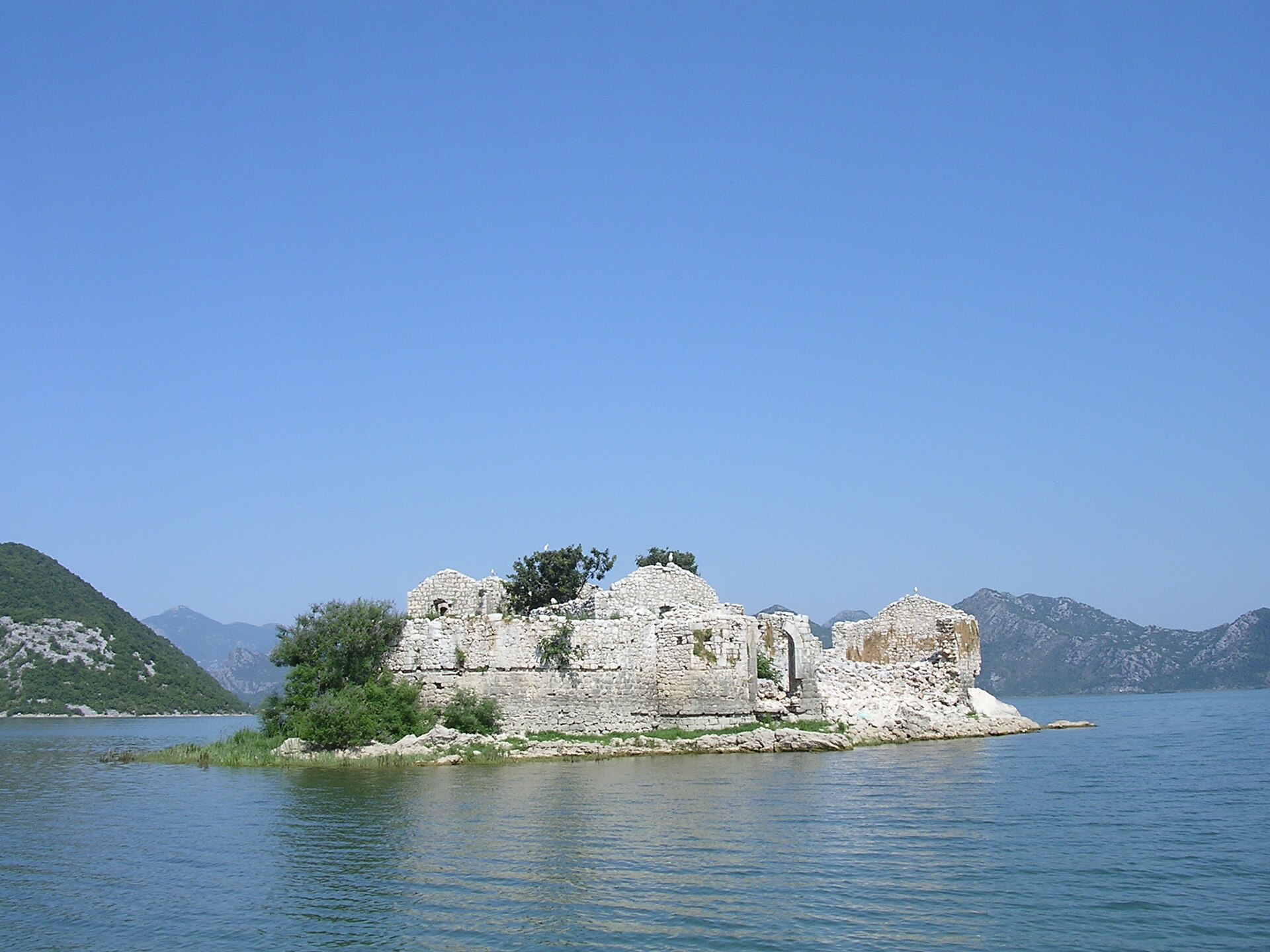 The ruined stone fortress of Grmožur on a small rocky island in Lake Skadar, low walls and scrub above the waterline