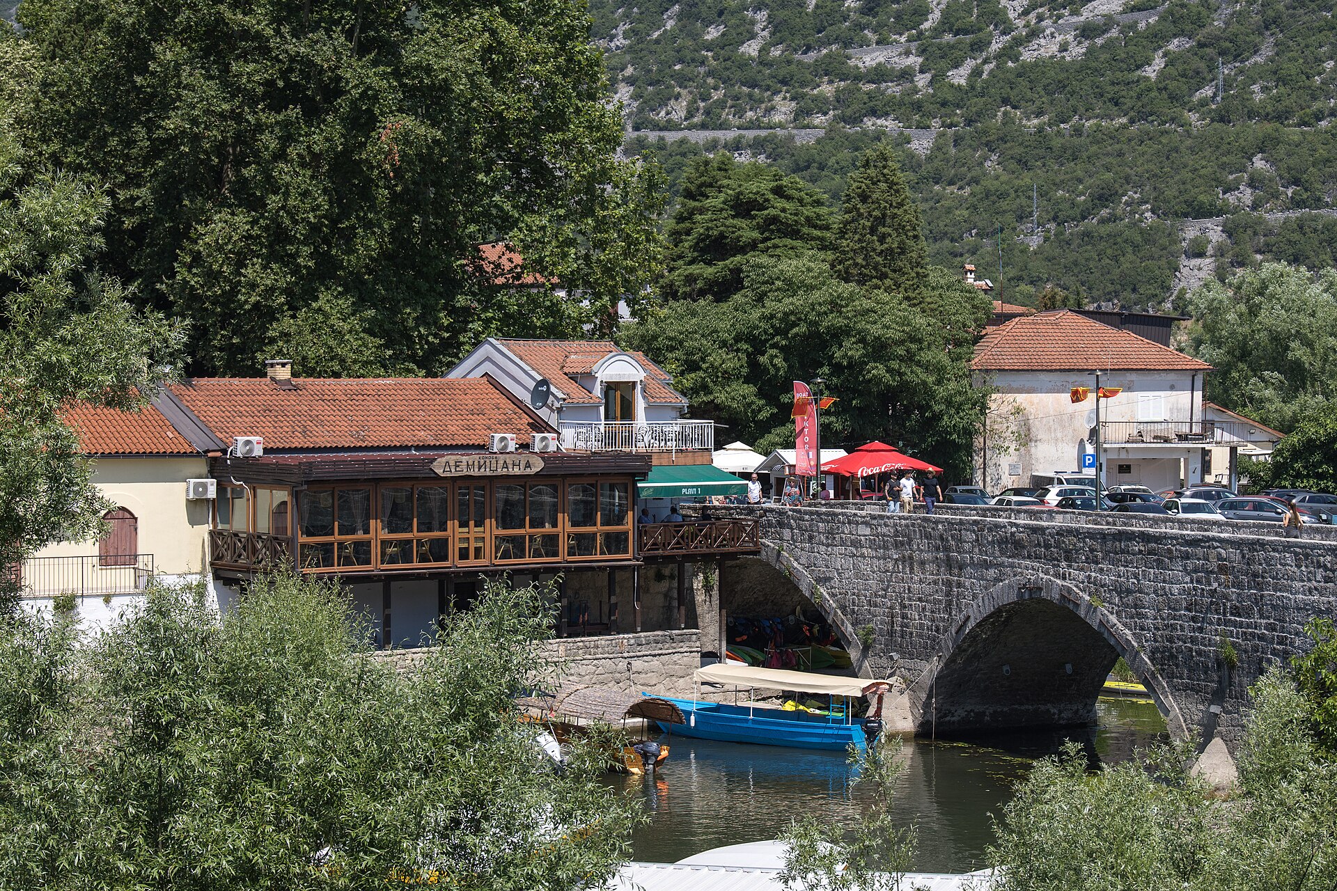 The village of Virpazar on Lake Skadar, an old stone bridge over the river with boats moored below and stone houses behind