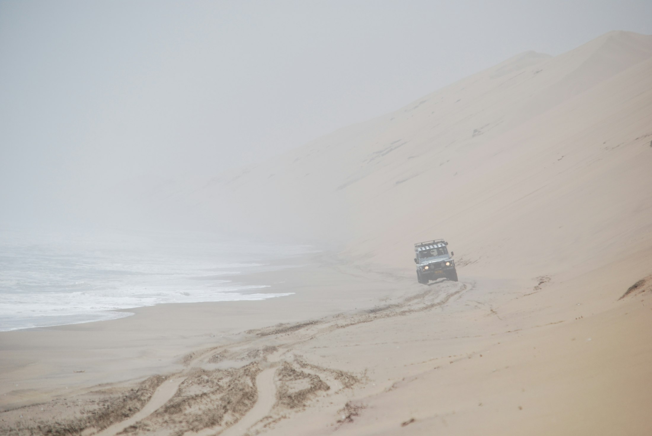 A single four-wheel-drive on the fog-bound beach below a Namib dune on the Skeleton Coast