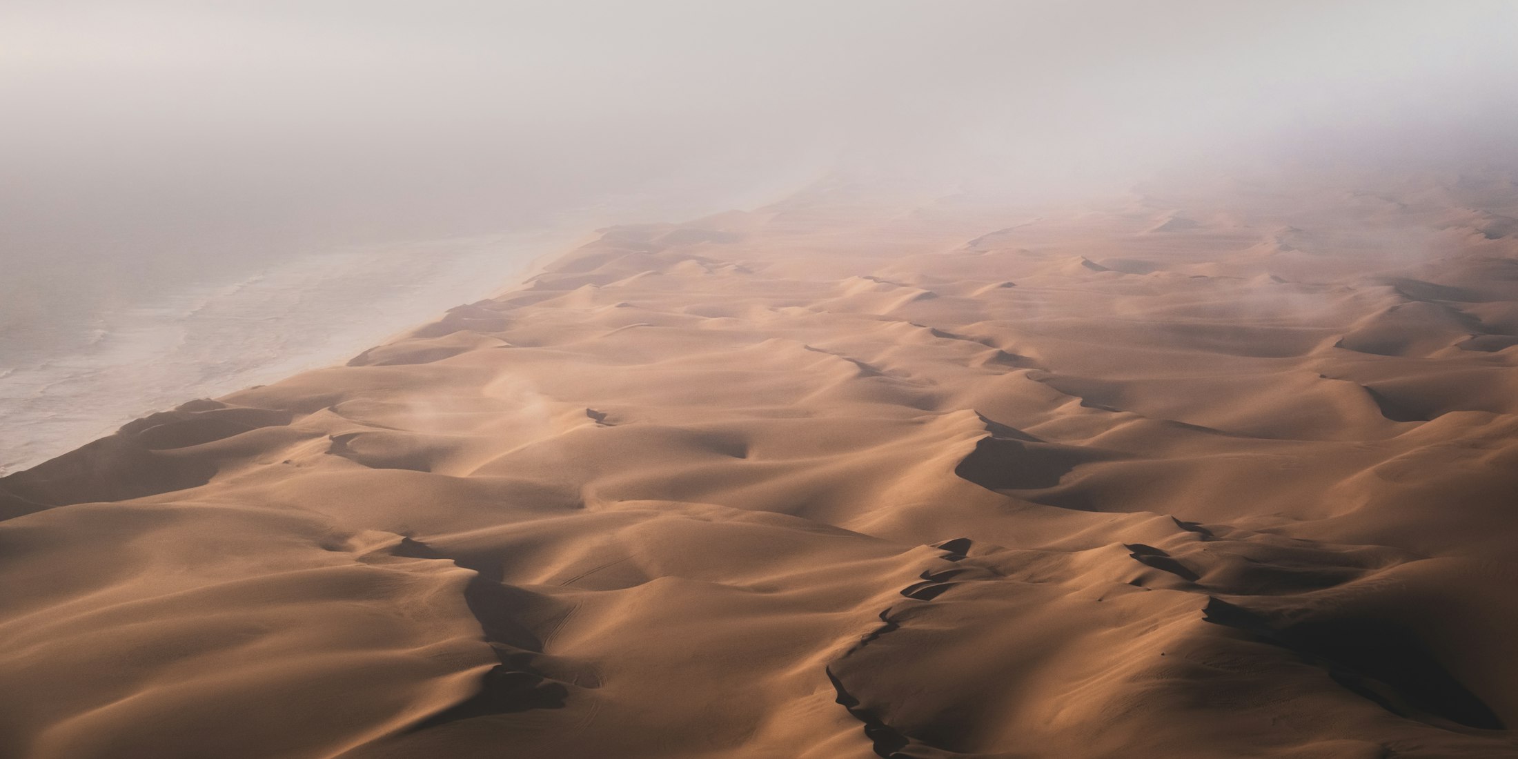 Fog from the cold Benguela current rolling over the dunes of the Namib where they meet the Atlantic