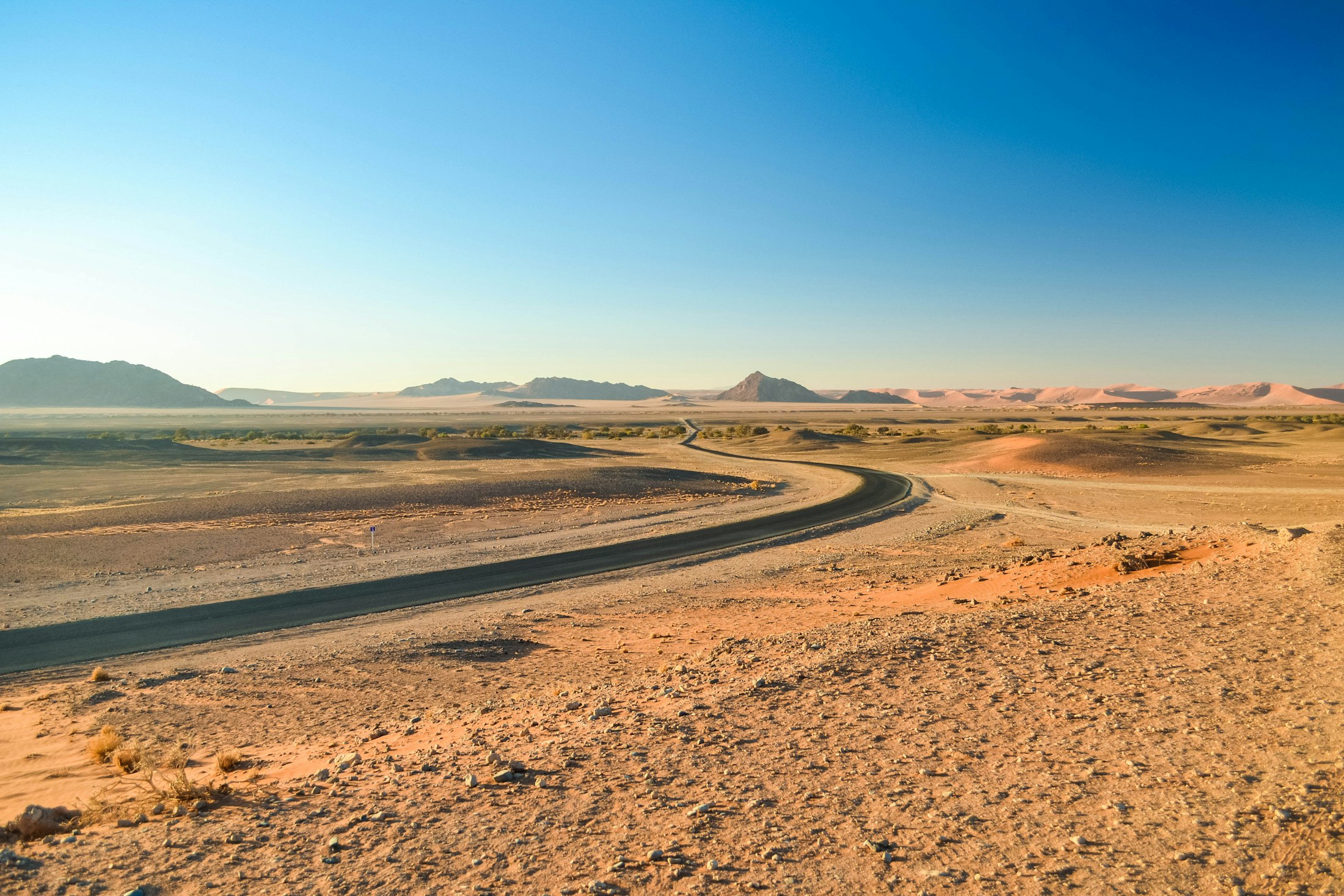 A gravel road curving inland across the Namib toward distant mountains and dunes