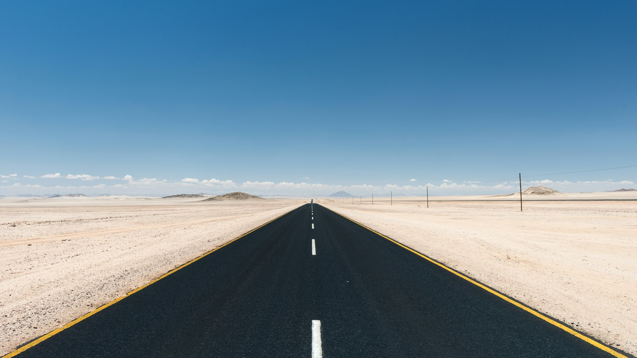 A dead-straight empty road running to the horizon across the flat Namib desert under a bare sky