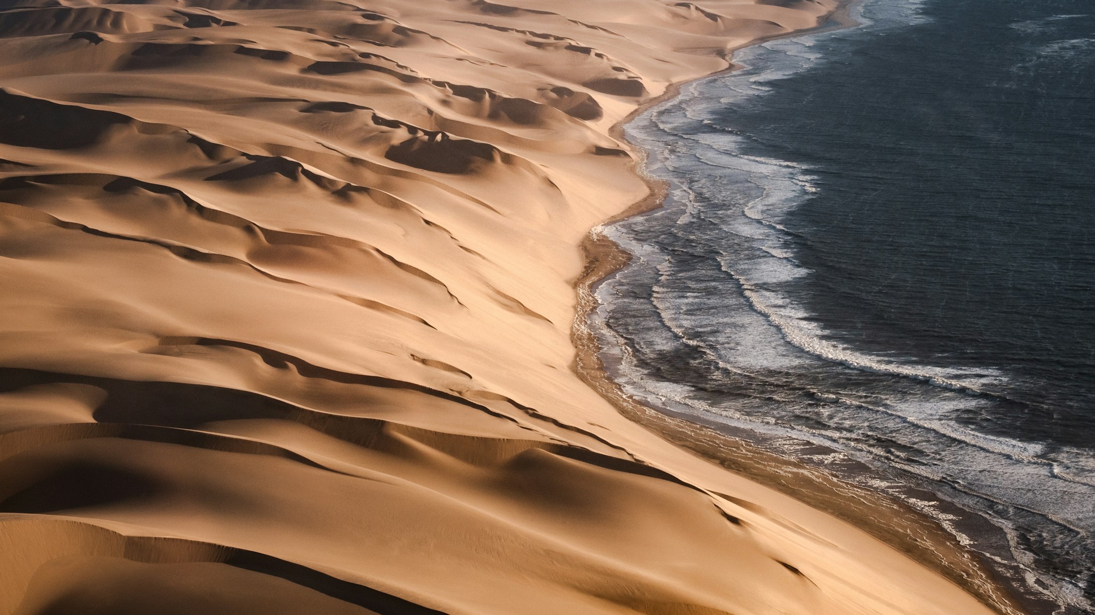Aerial view of the Namib dunes pouring straight down into the cold Atlantic surf