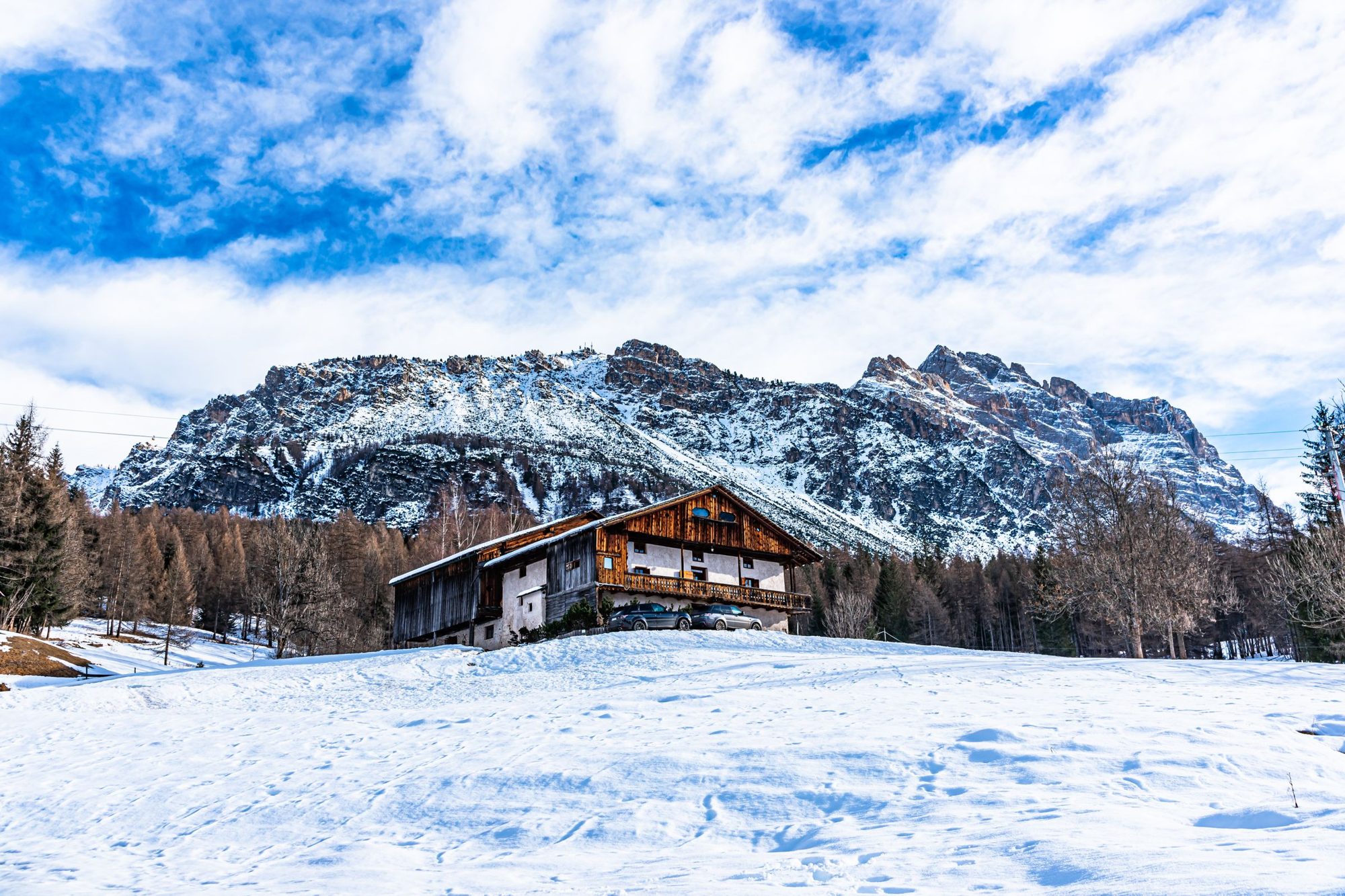 A wooden hut in a snowy meadow above Cortina, with mountains behind