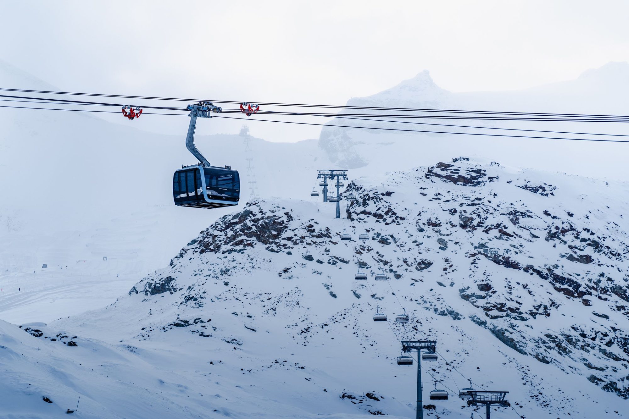 A gondola and chairlifts over snow-covered rock on the upper mountain above Zermatt